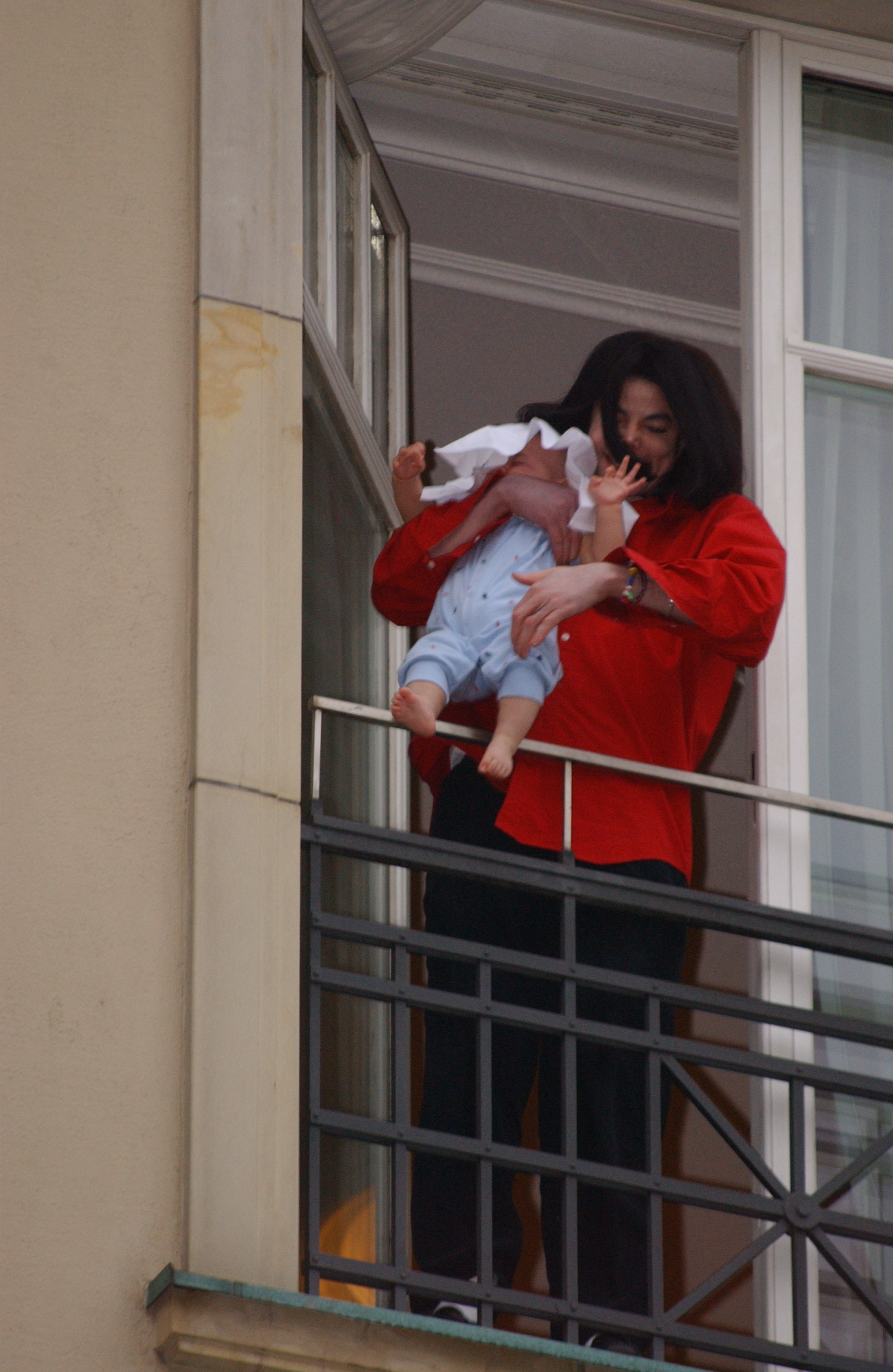 Michael Jackson stands on a balcony, holding Bigi Jackson at Hotel Adlon in Berlin, Germany on November 19, 2002.