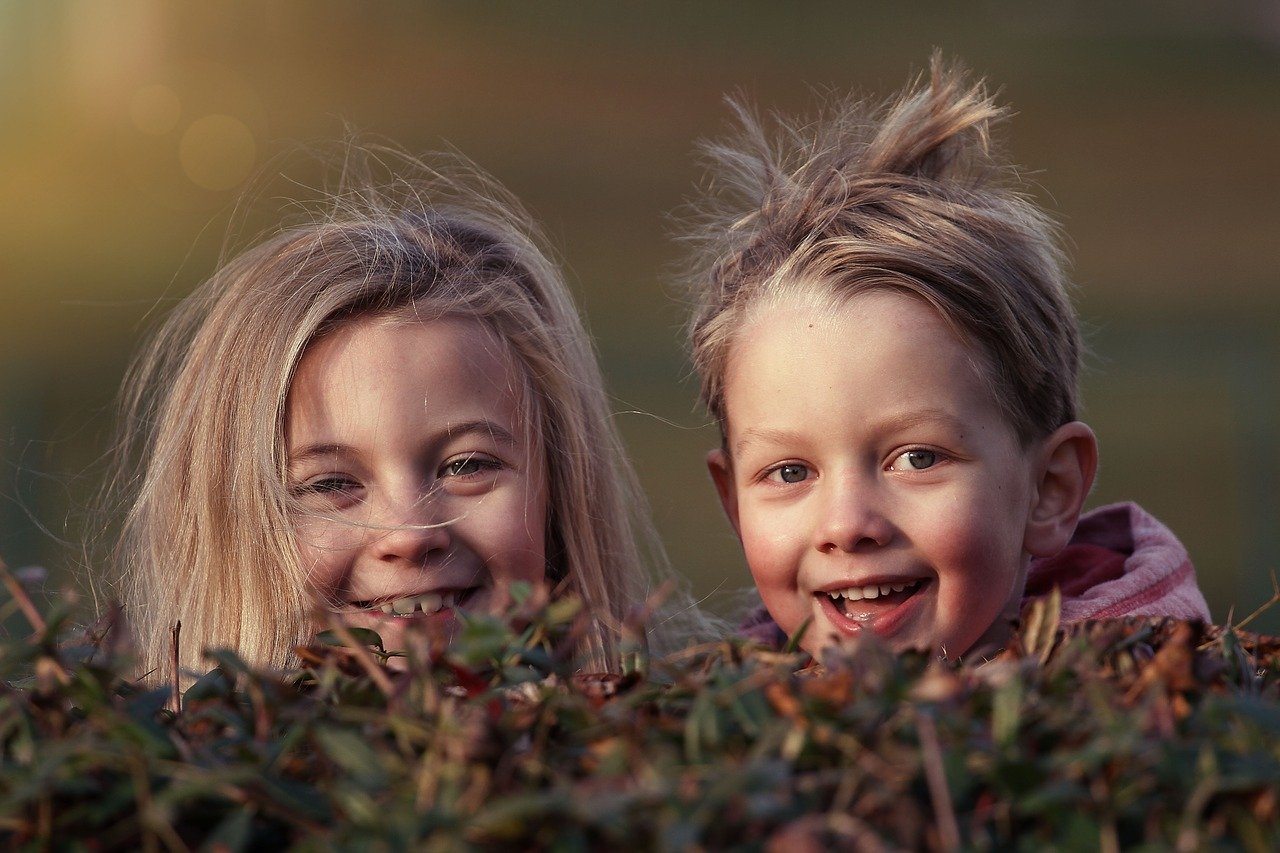 Two children smiling while looking ruffled up while playing in the bushes | Photo: Pixabay/Lenka Fortelna