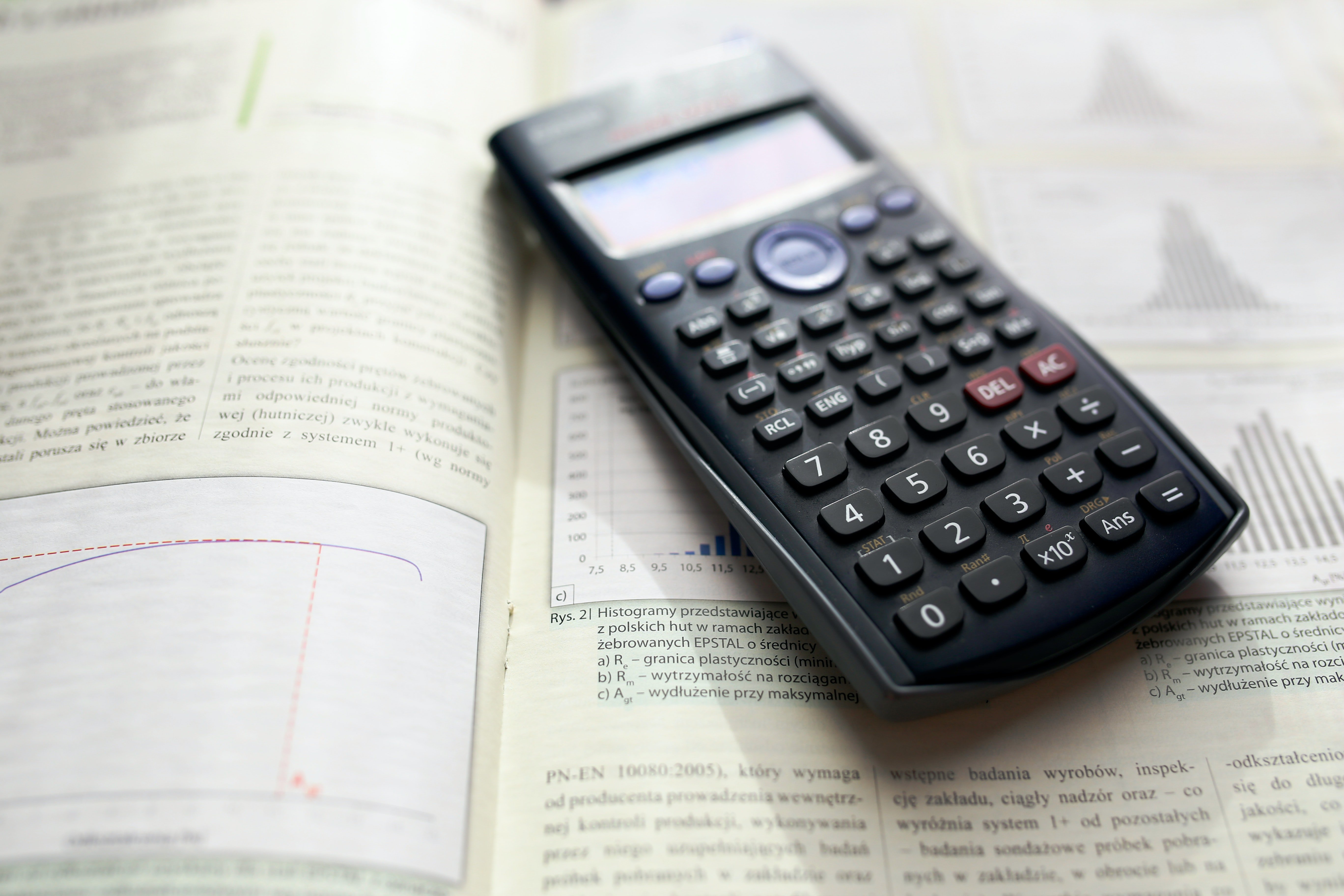 A calculator on top of an open textbook. | Pexels/ Kaboompics .com