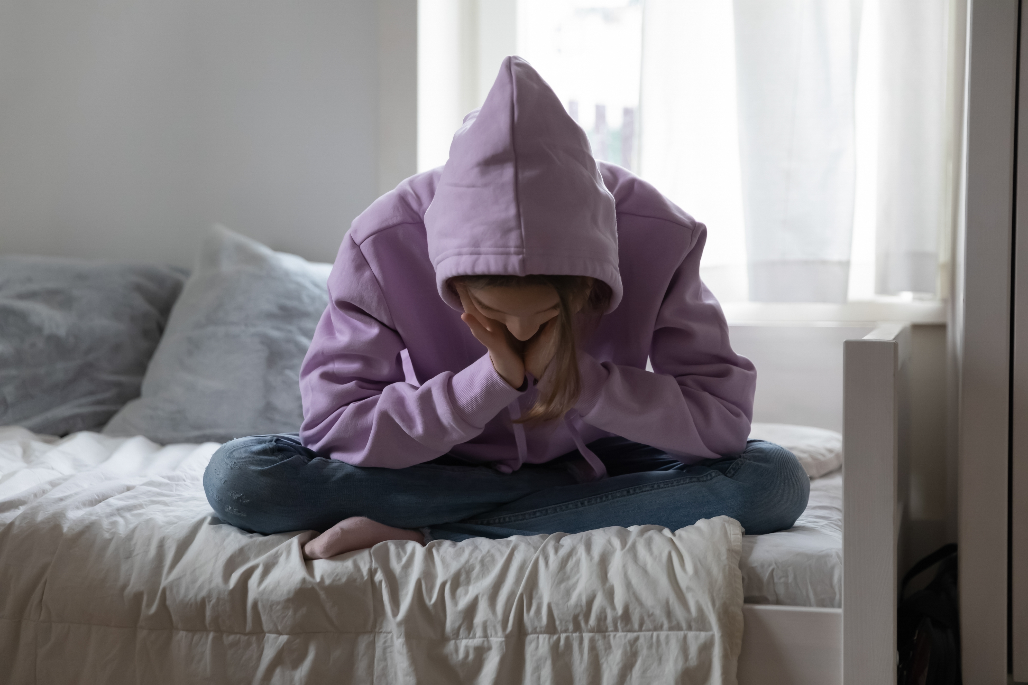 An young girl in a hoodie sitting on a bed  Source: Shutterstock