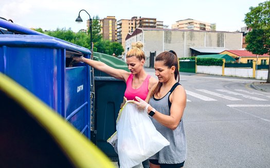 Photo of two girls throwing garbage to recycling dumpster | Photo: Getty Images