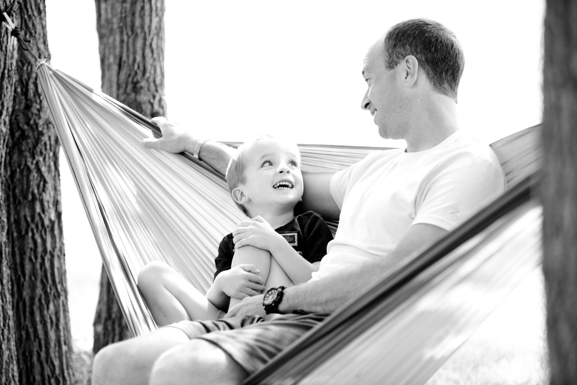 A grayscale photo of a father and son sitting on a hammock | Source: Pexels