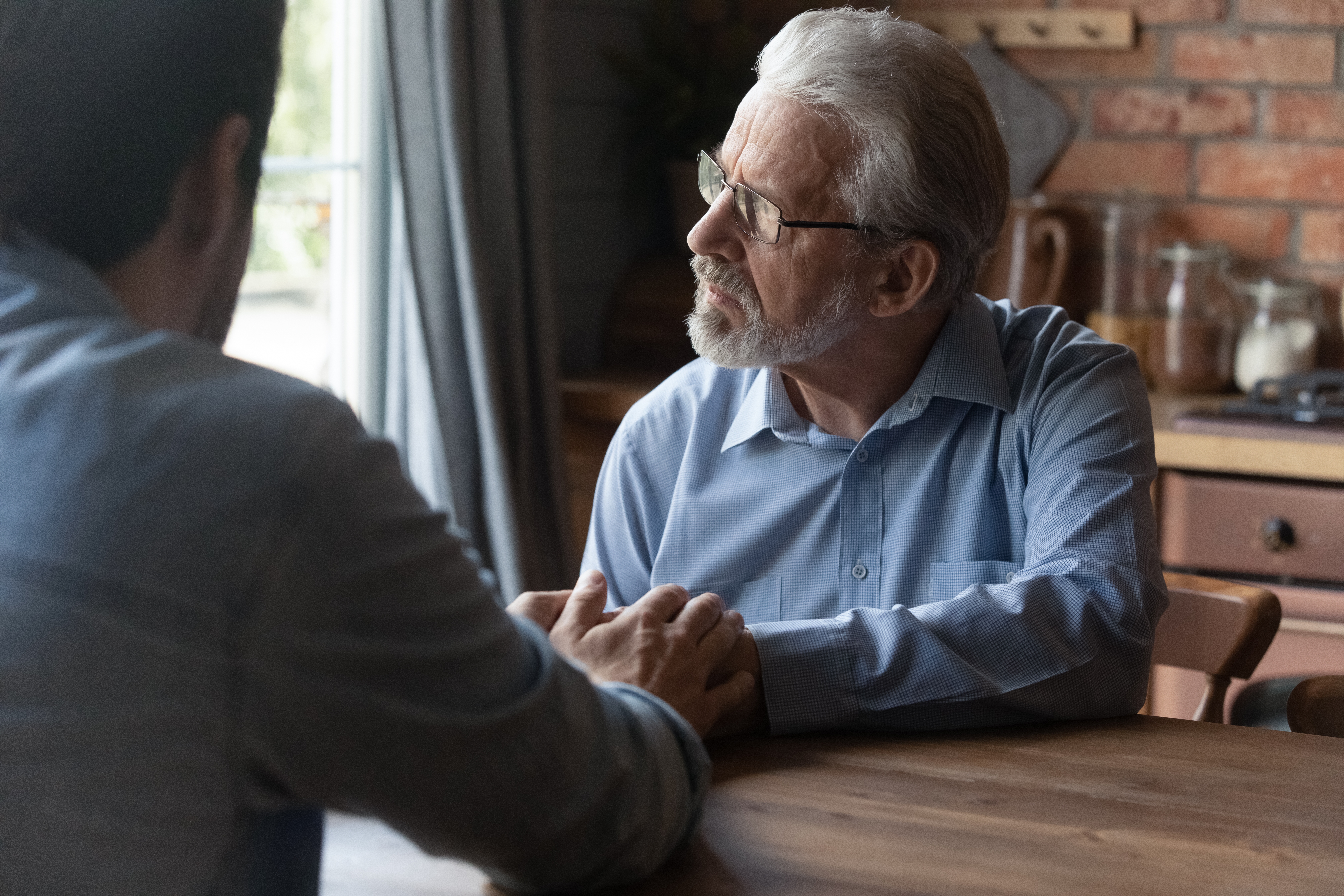 An adult son sitting with his stressed father | Source: Shutterstock