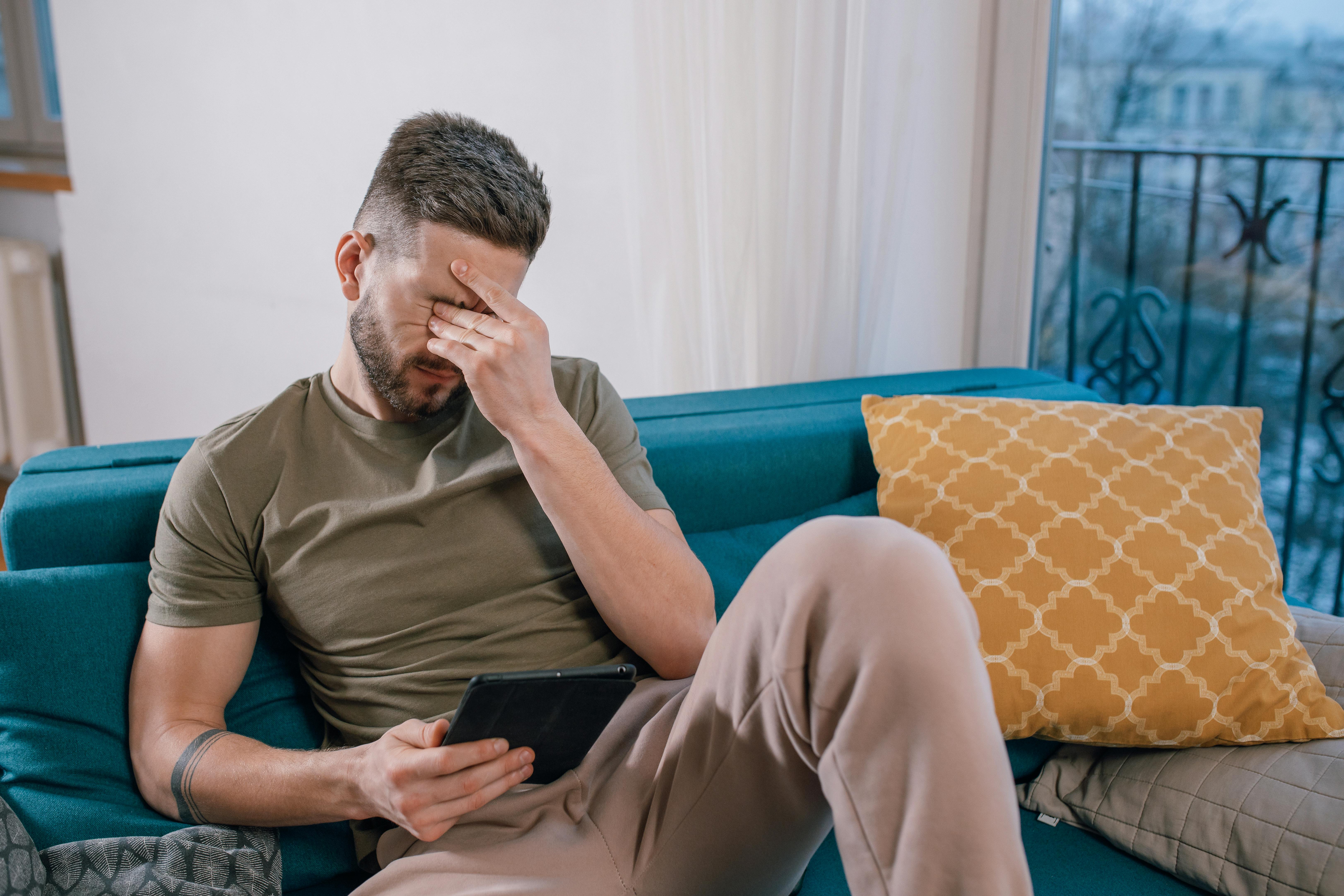 A man crying while sitting and looking at something on a tablet | Source: Pexels
