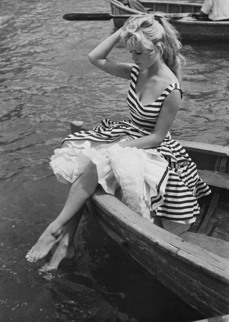 Vue de l'actrice française Brigitte Bardot, dans une robe rayée, assise à la proue d'une barque et plongeant ses pieds dans l'eau, années 1950 | Photo : Getty Images