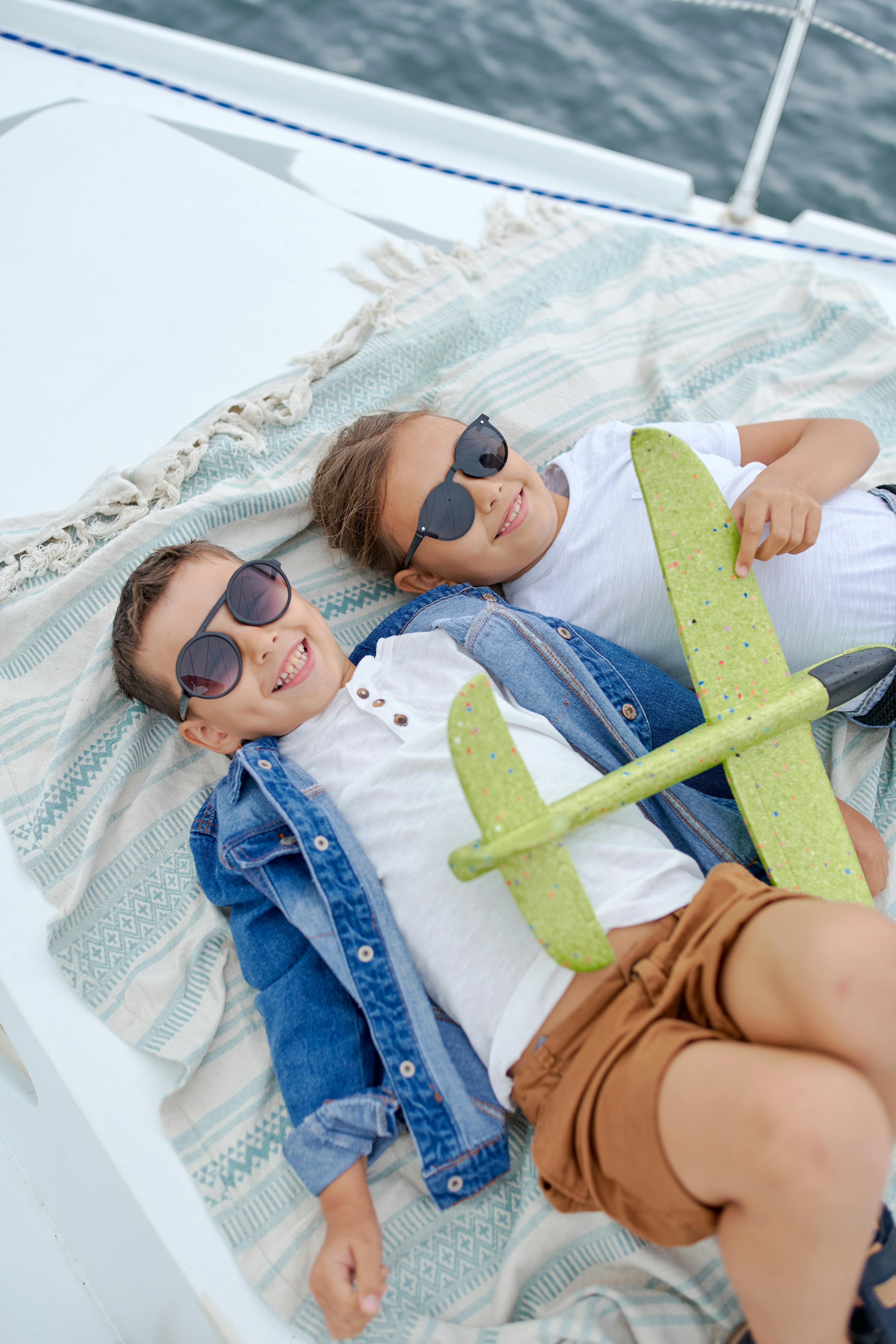 Two happy children lying facing up on a boat playing with a toy plane | Source: Pexels