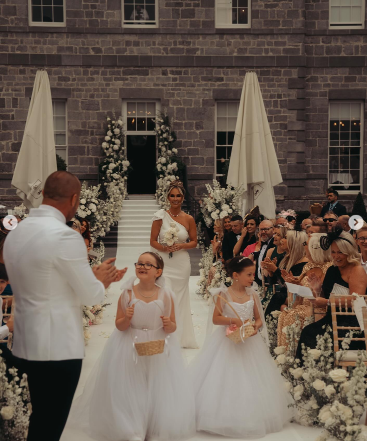 Terry Kavanagh applauds as Croia McGregor, another unnamed flower girl, and Dee Devlin make their way down the aisle on August 17, 2024 | Source: Instagram/thenotoriousmma