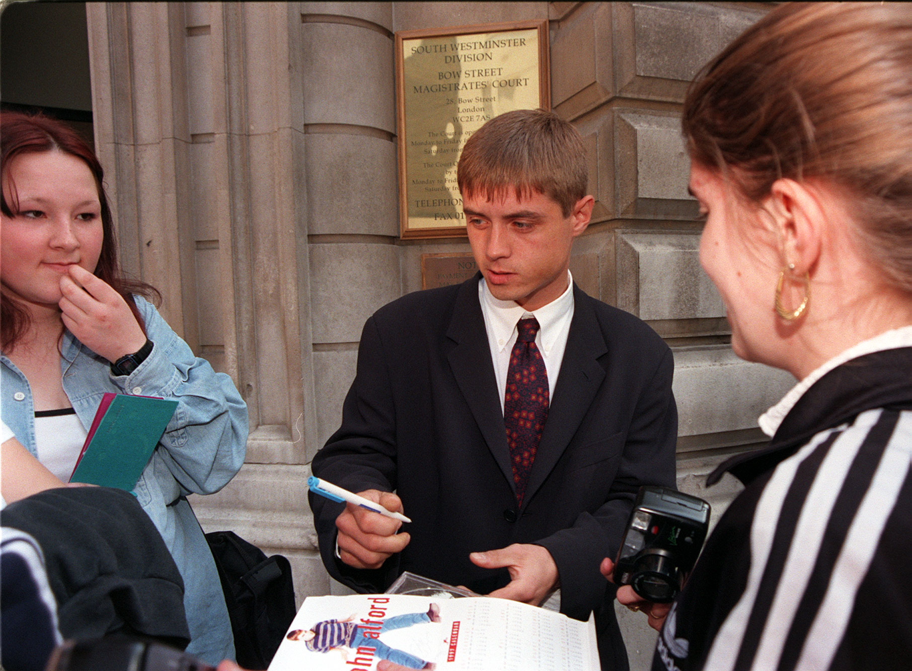 John Alford signs autographs for fans outside Bow Street Magistrates court in London on 15 May 1998, where he was remanded on bail after being charged with supplying cocaine. | Source: Getty Images