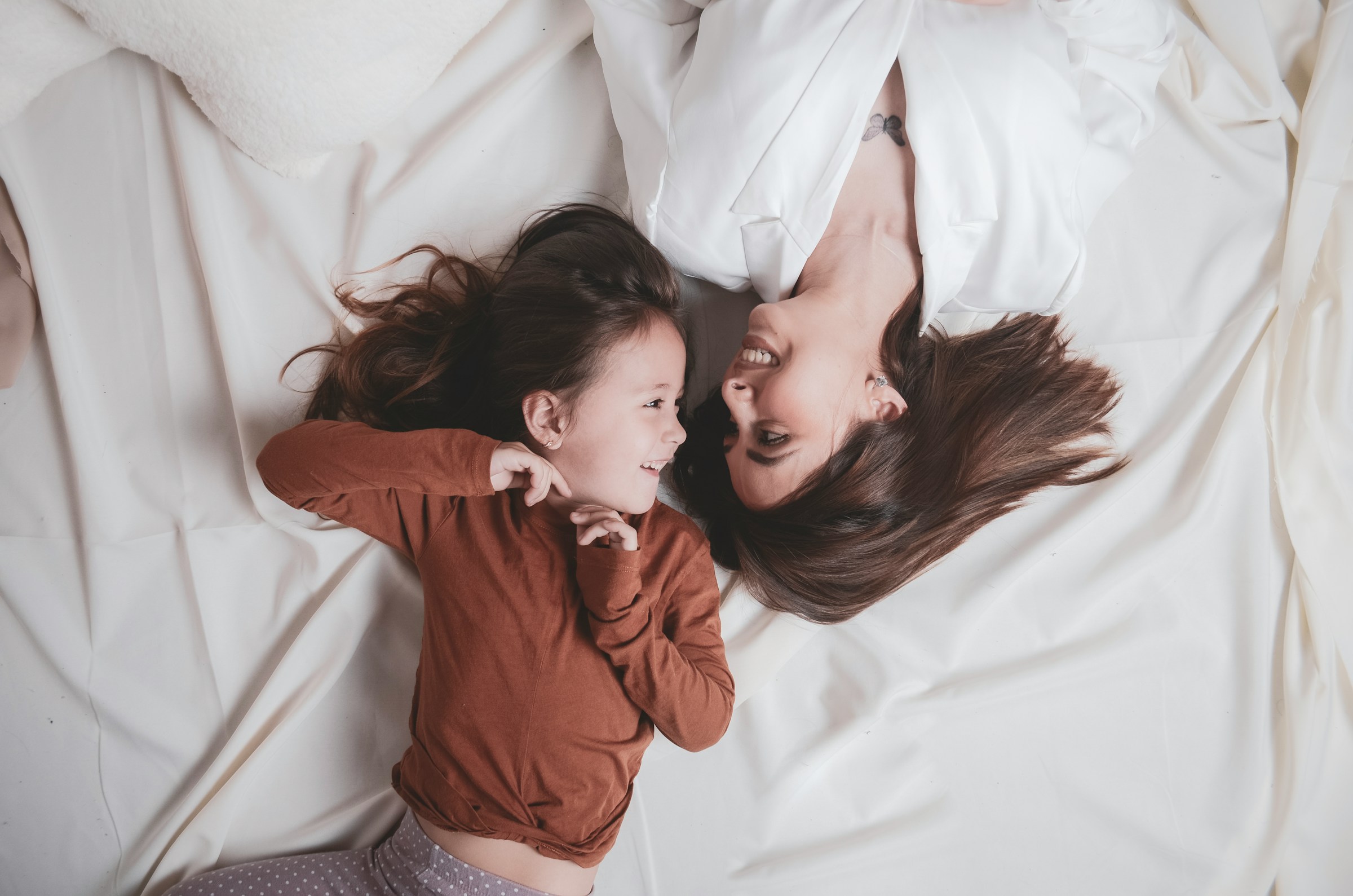 A woman and a little girl looking at each other while lying in bed | Source: Unsplash