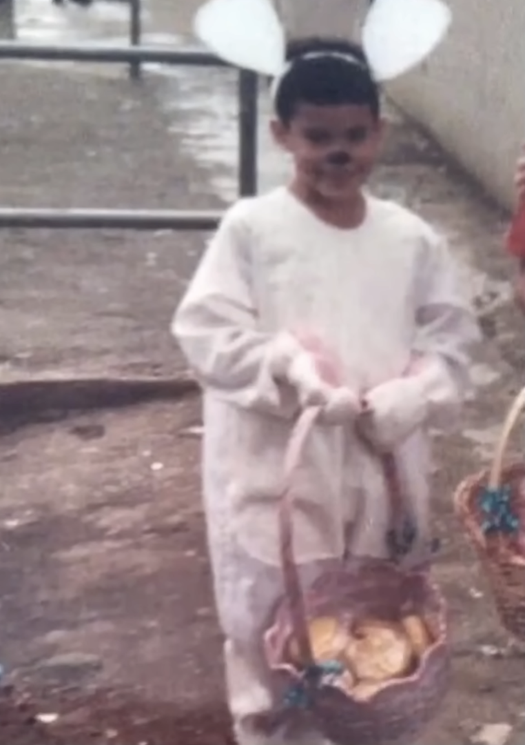 A young Bad Bunny wears a bunny costume and a half-full basket, A young Bad Bunny smiles at the camera as he sits in a chair, from a post dated August 31, 2025. | Source: YouTube/TODAY