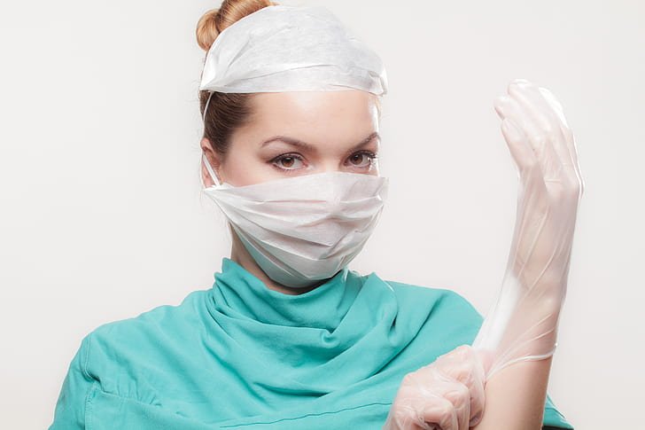 Doctor in scrubs wearing a latex glove and a face mask | Photo: PickPik