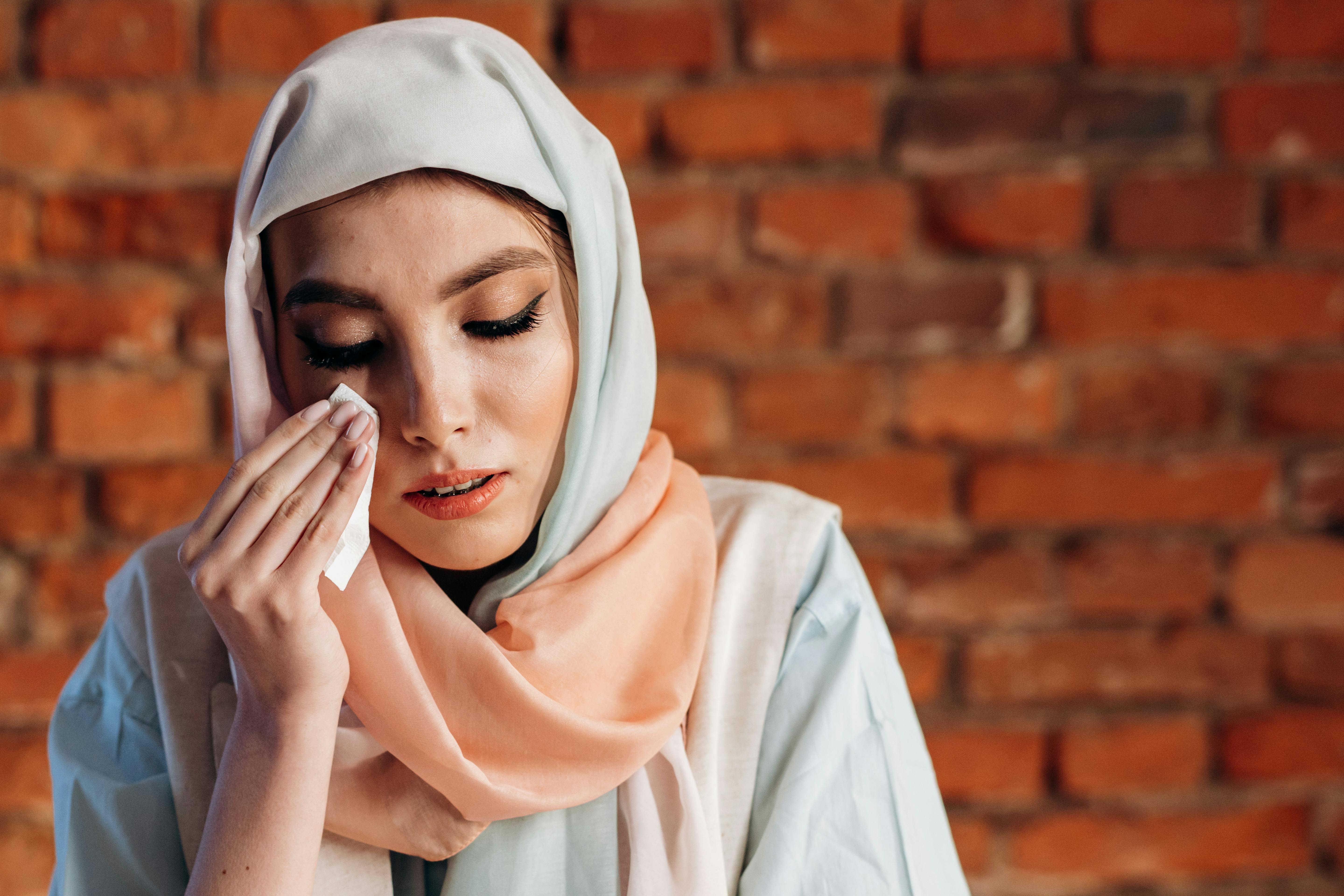 A sad woman wiping away her tears with a scarf | Source: Pexels