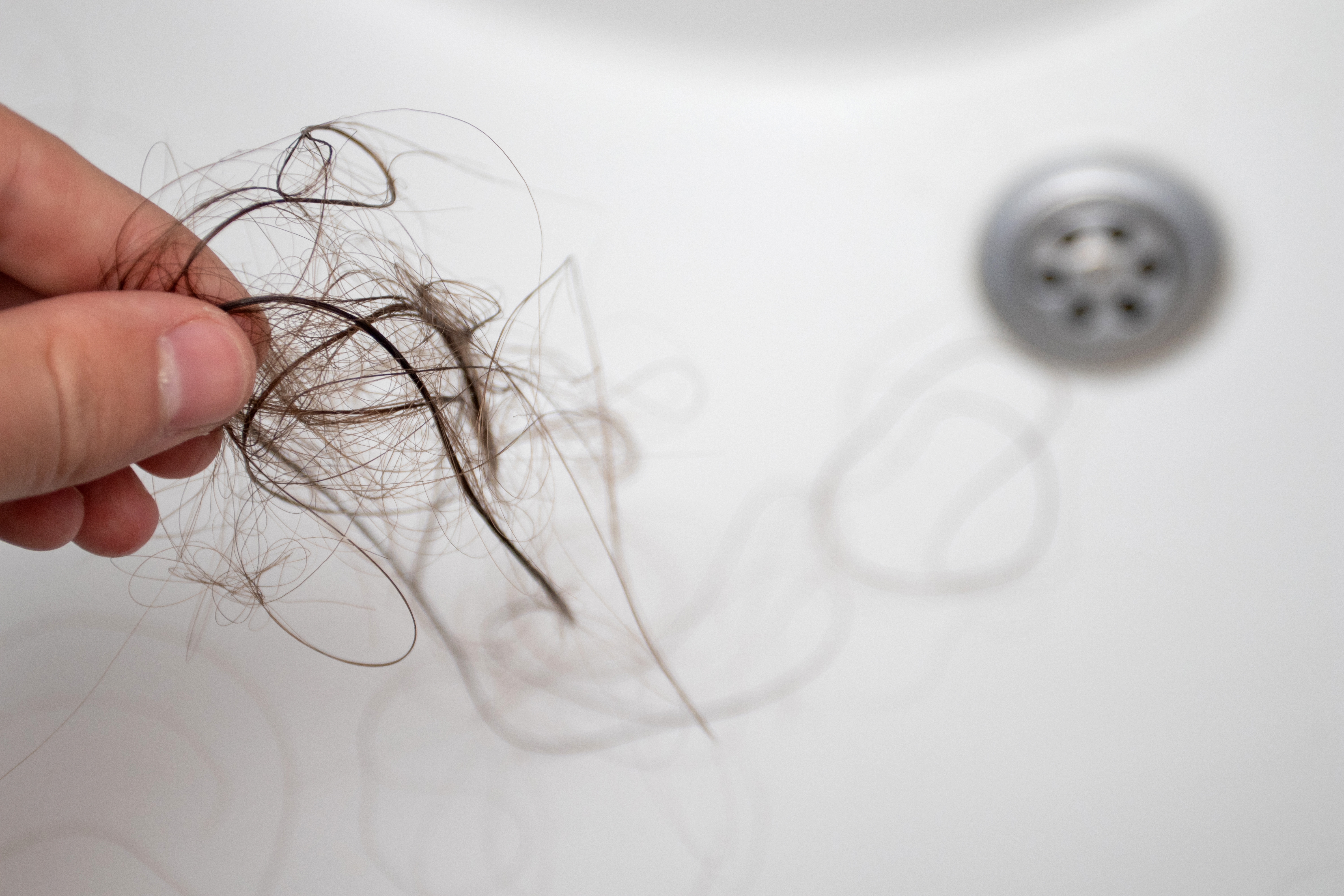 A person holding a bunch of hair strands above a sink | Source: Shutterstock