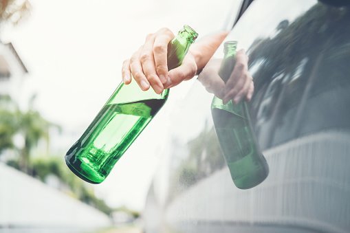 A cropped image of a man in a car holding a bottle of beer.| Photo: Getty Images.