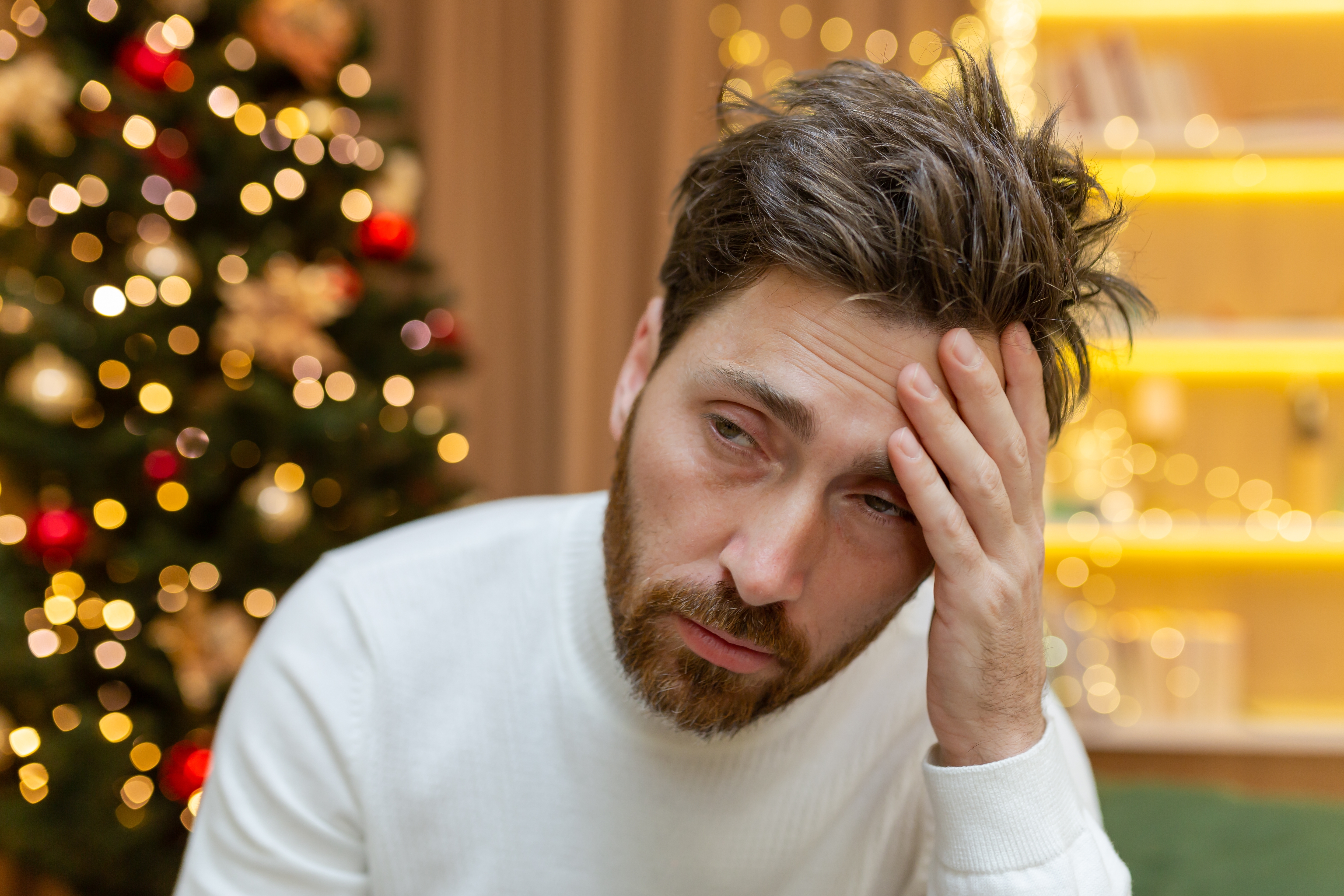A depressed man sitting near a Christmas tree at home | Source: Shutterstock