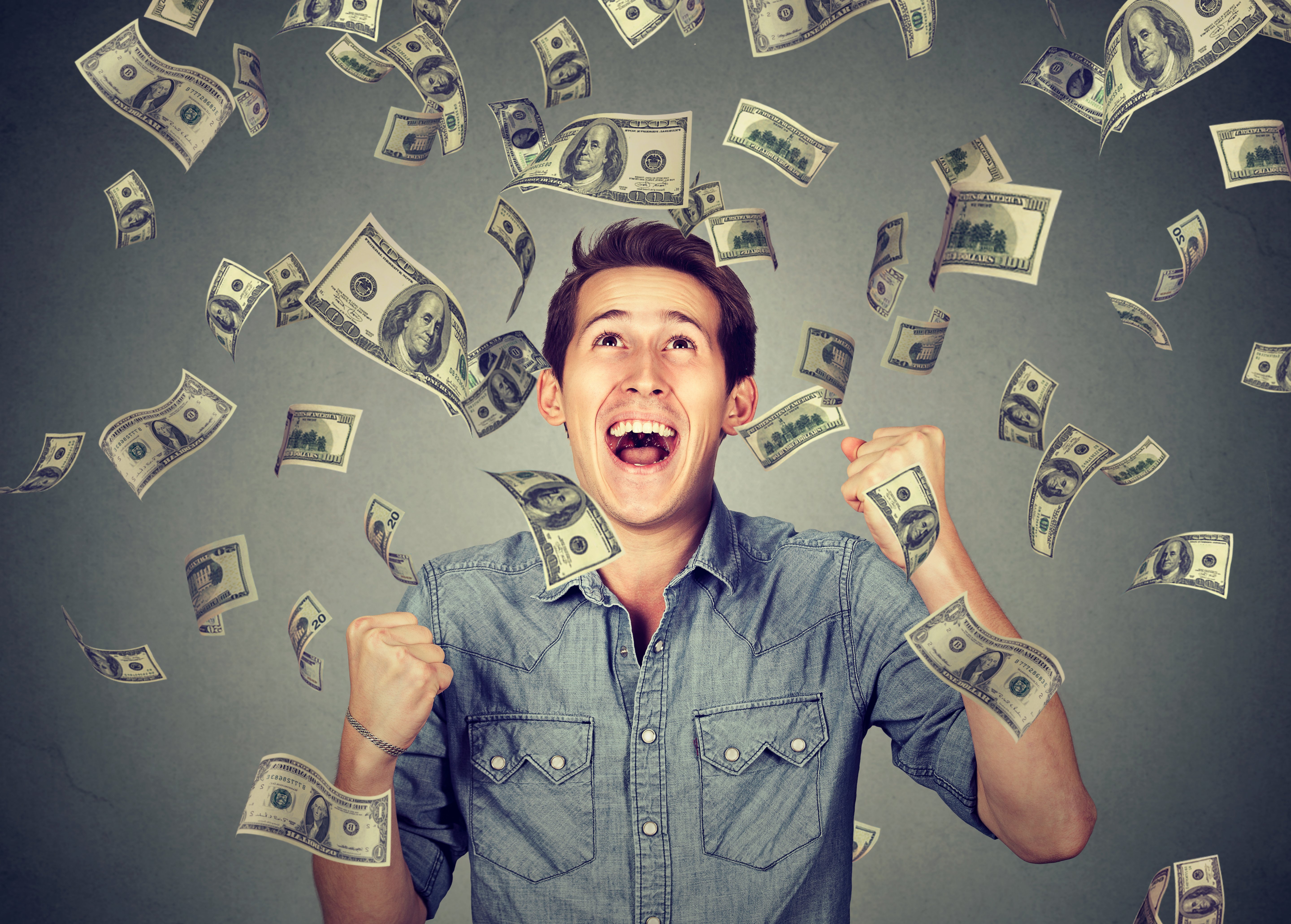 A happy man celebrates under dollar bills raining down from above. | Photo: Shutterstock. 