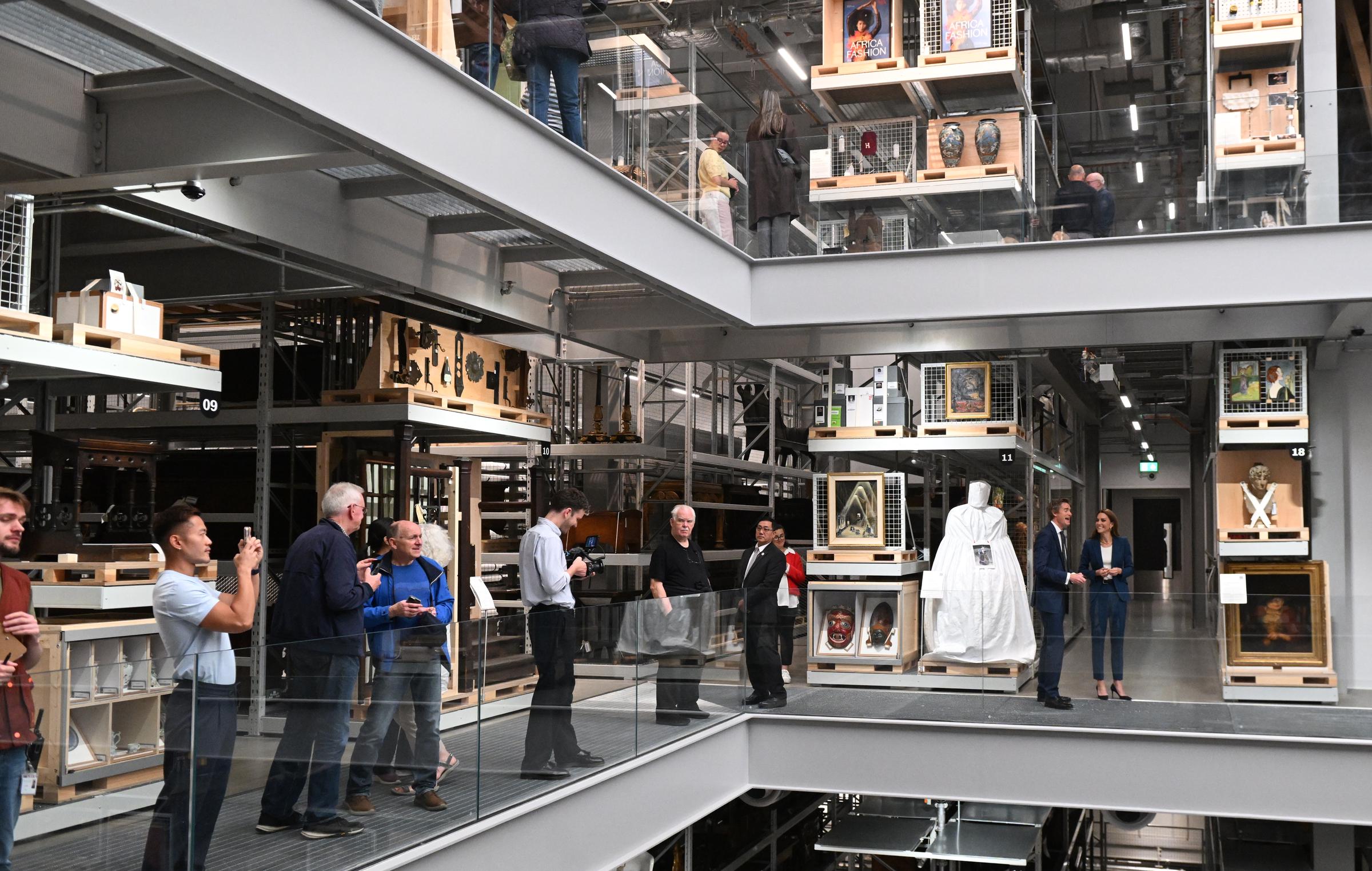 Amid a busy backdrop of visitors and staff, Princess Catherine walks with Tristram Hunt inside the V&A East Storehouse. Dressed in a royal blue suit, she appears composed and attentive as she tours the striking multi-level gallery space.