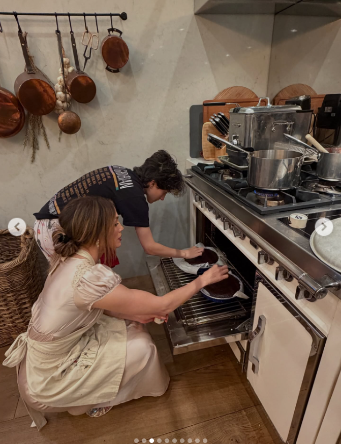 Jennifer Lopez and the young person beside her check on the cakes in the oven, as seen from a post dated November 28, 2025. | Source: Instagram/jlo