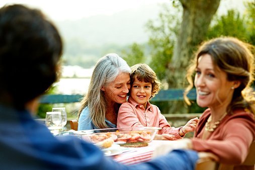Happy grandmother sitting with grandson and family at outdoor meal table in yard | Photo: Getty Images