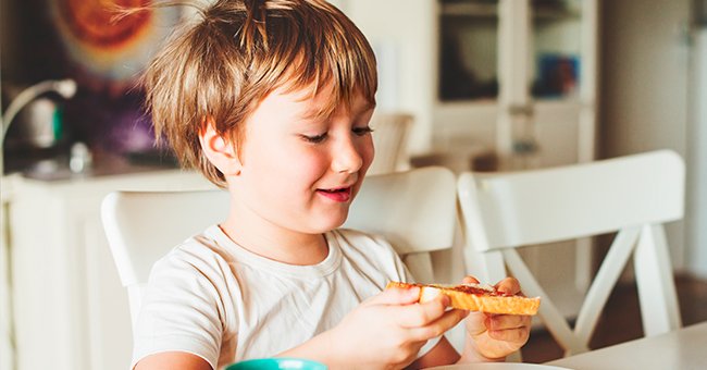 A child holding a slice of bread on the table. | Source: Shutterstock