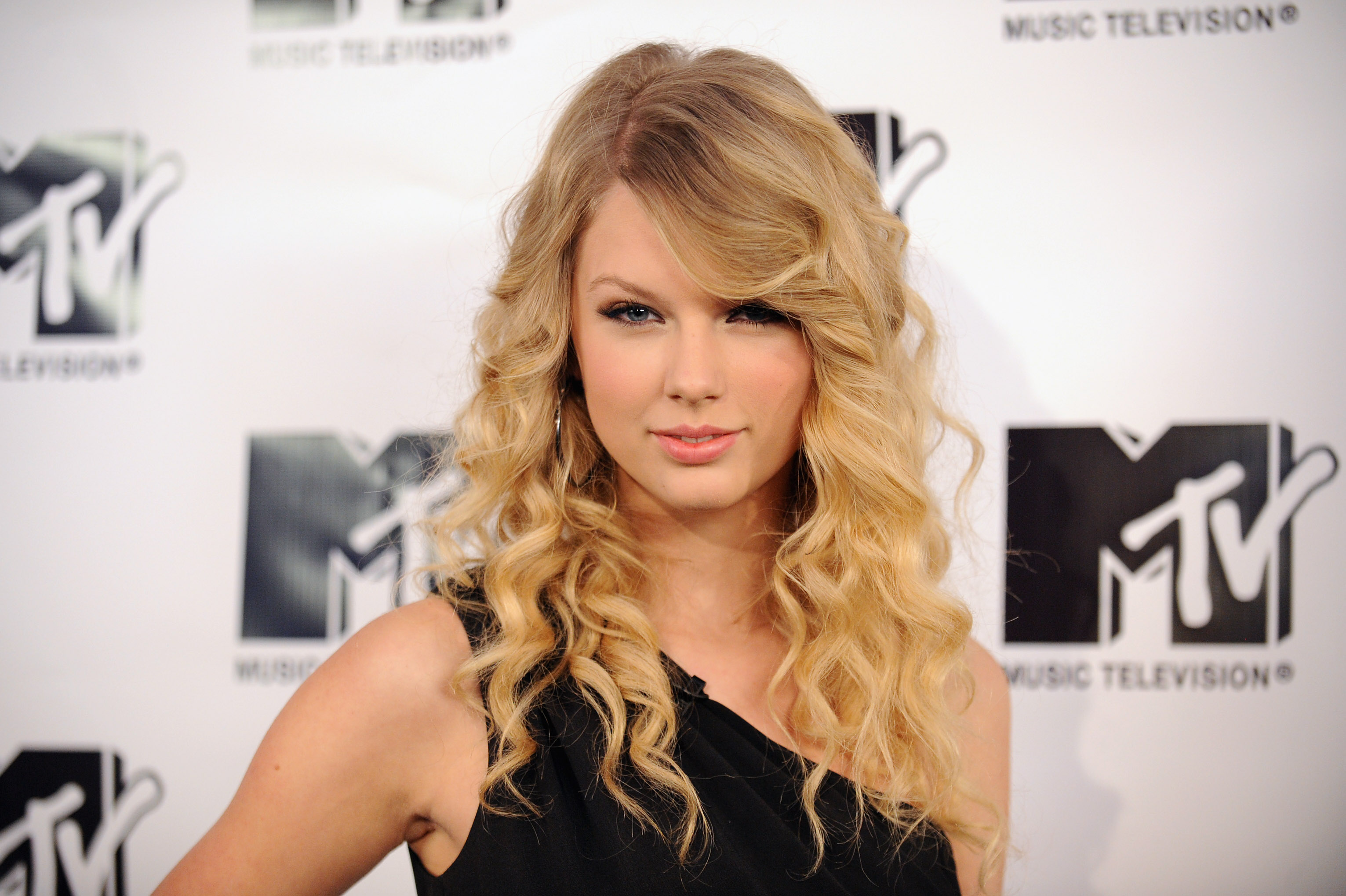 Musician Taylor Swift attends MTV's TRL "Total Finale Live" at the MTV studios in Times Square. Wearing a one-shoulder black dress and voluminous curls, she exudes confidence as she bridges her country roots with pop stardom.