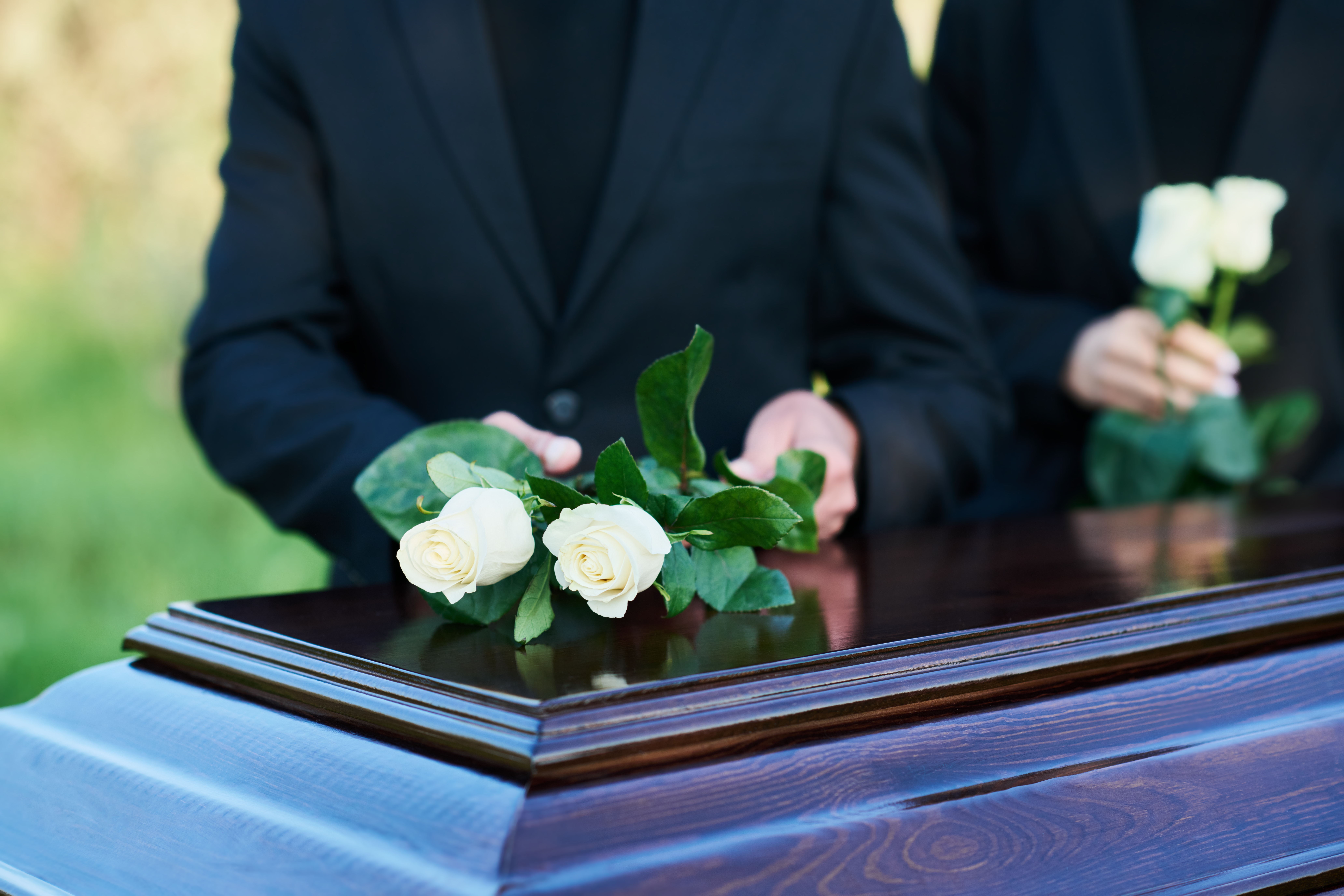 People placing white roses on a coffin | Source: Shutterstock