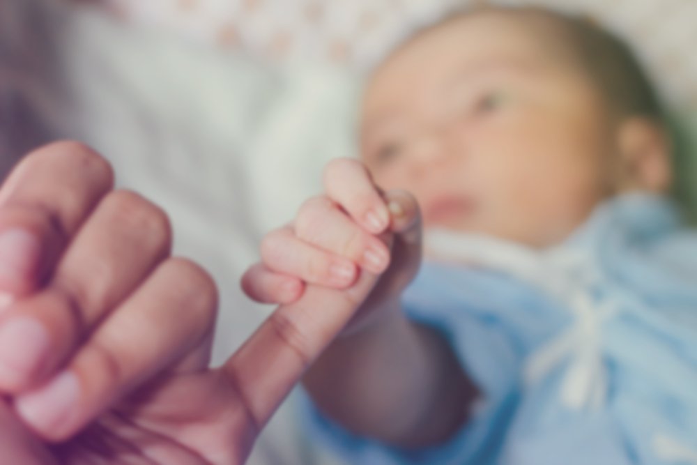 A blurred photo of a newborn baby holding its mother's hand. | Photo: Shutterstock