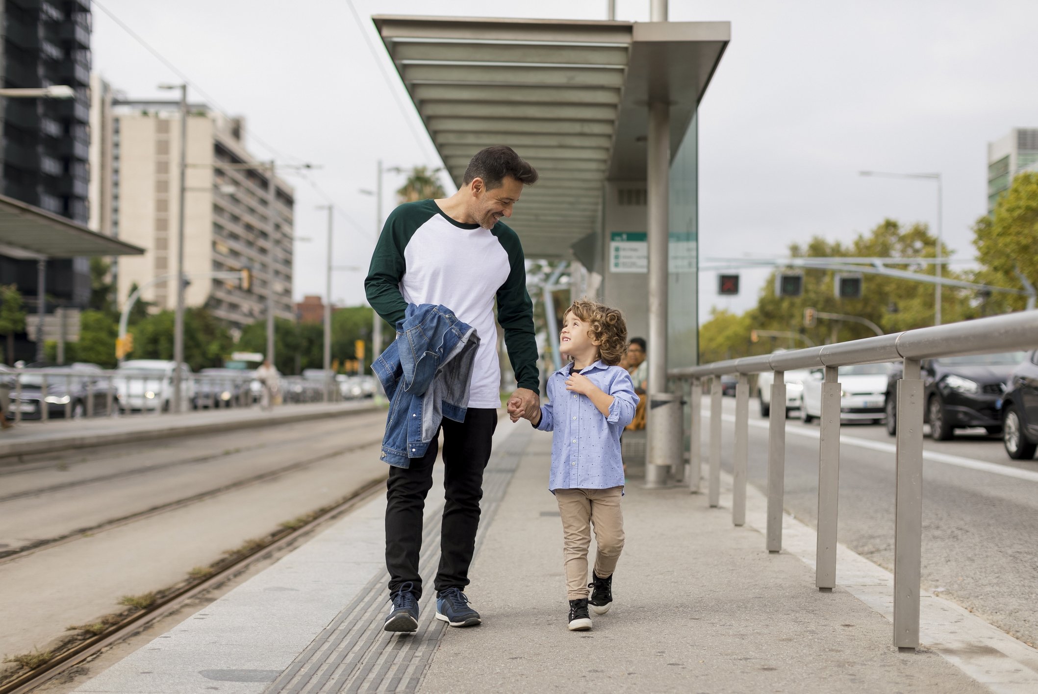              Smiling father and son walking hand in hand at tram stop in the city : Stock Photo   Buy the print   Comp   Smiling father and son walking hand in hand at tram stop in the city  | Photo: Getty Images