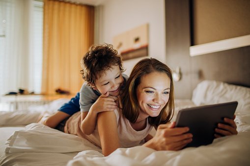 A mother and her son on the bed looking at a tablet.| Photo: Getty Images.