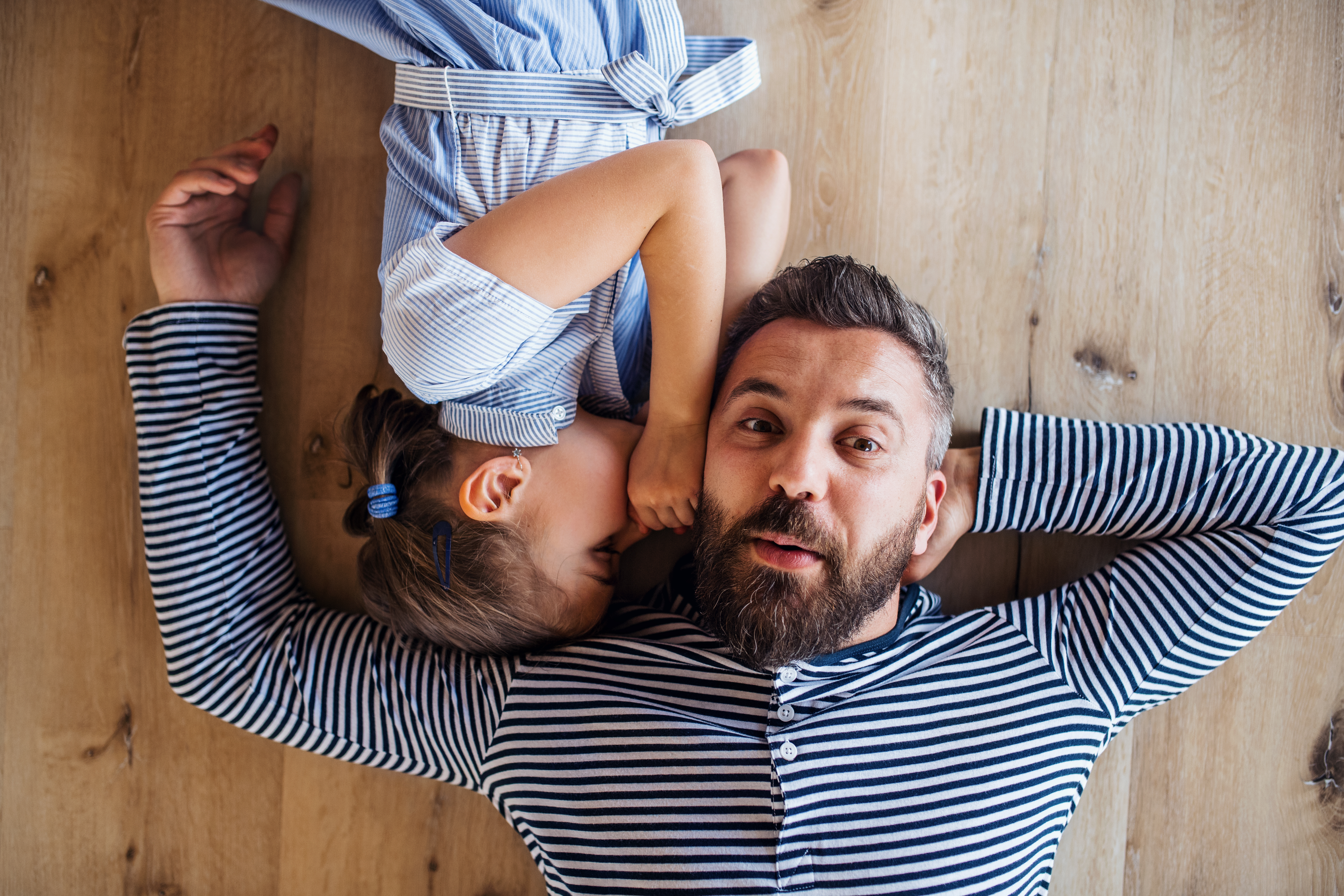 Top view of mature father and small daughter lying on floor indoors at home, whispering | Source: Getty Images