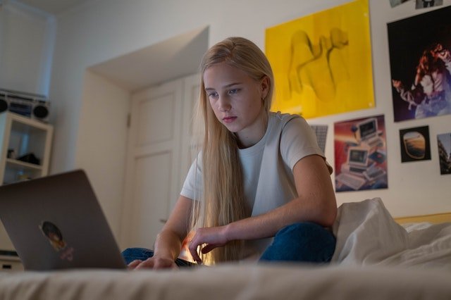 Teenage girl sitting on bed using a computer | Source: Pexels