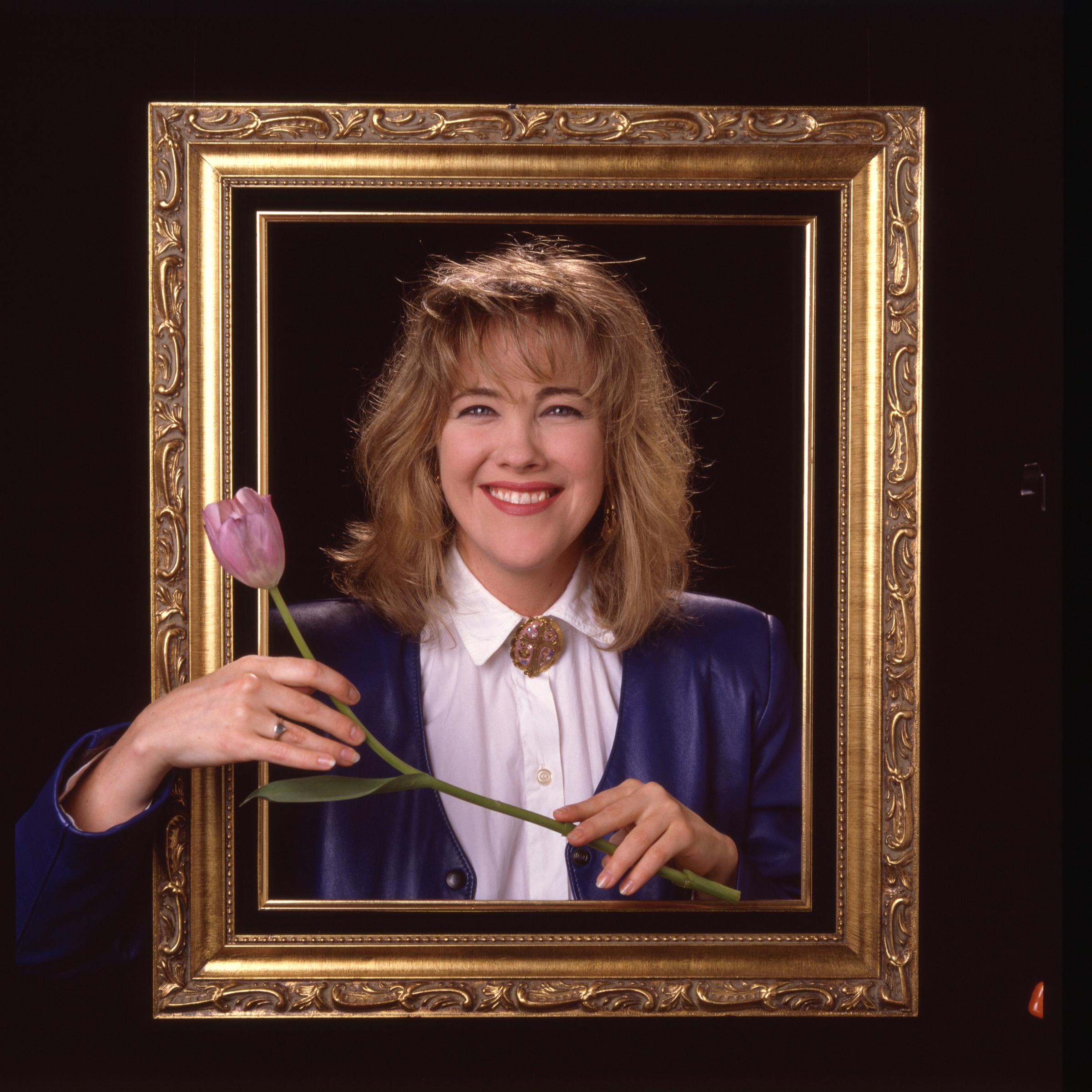 Catherine O'Hara smiles from behind an ornate gold frame while holding a tulip in 1986, in Los Angeles | Source: Getty Images