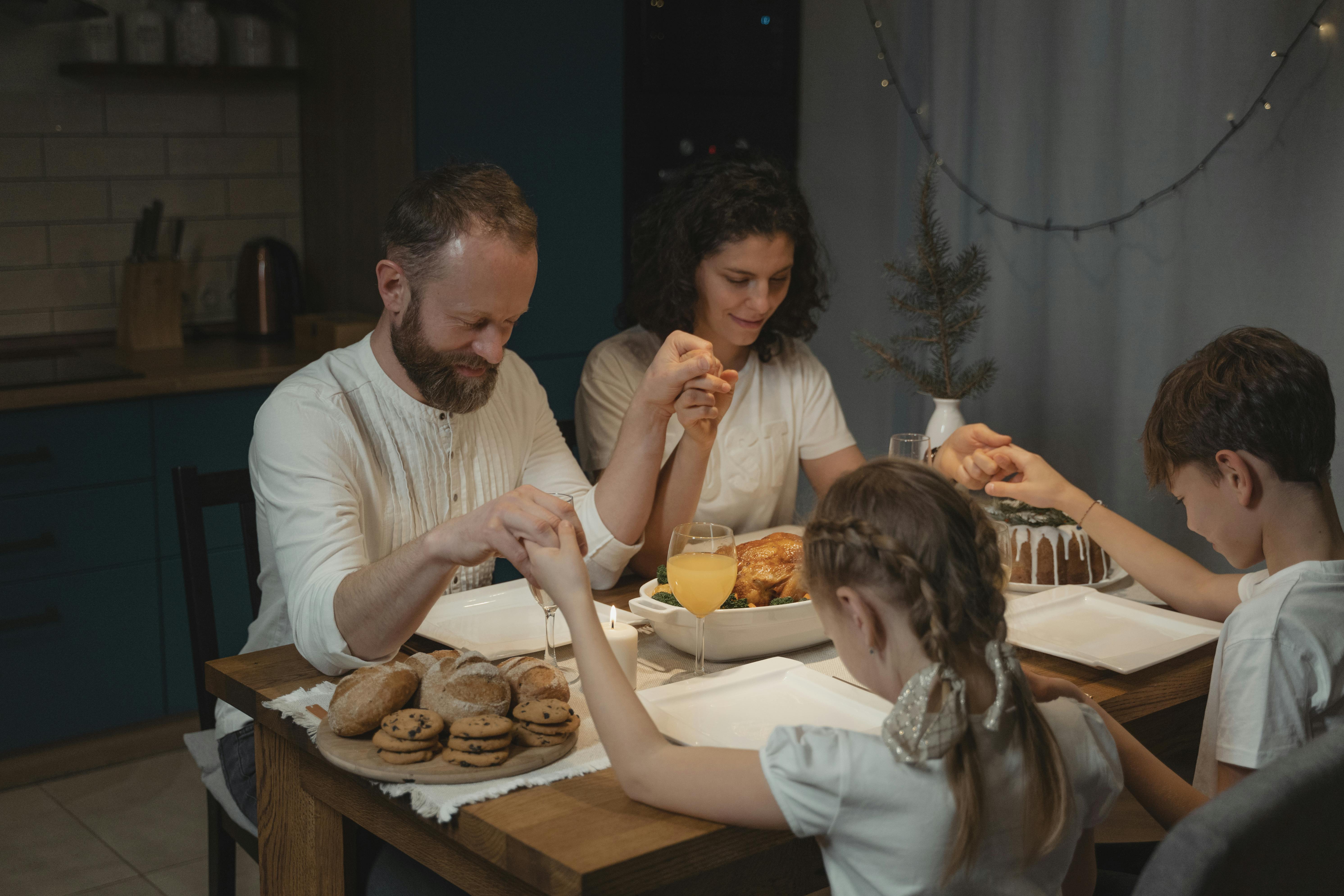 Parents holding their children's hands while praying before eating | Source: Pexels