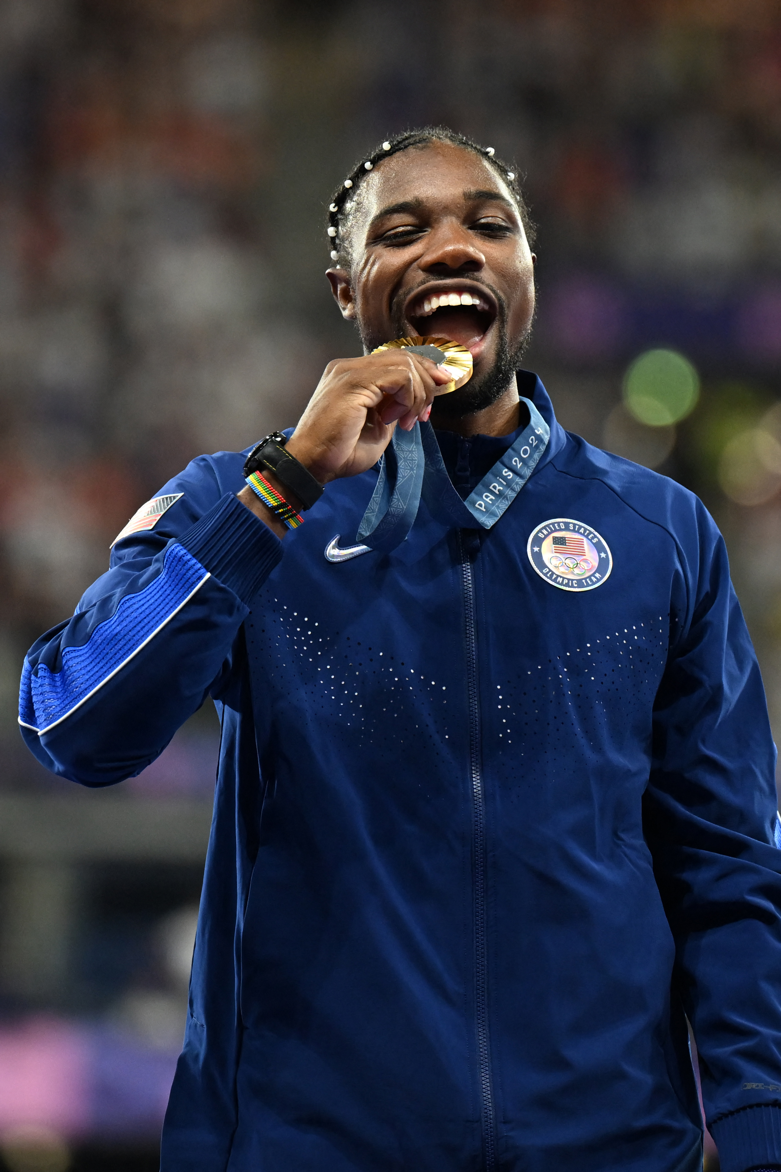 Noah Lyles celebrates on the podium during the victory ceremony for the men's 100m athletics event during the Paris 2024 Olympic Games at Stade de France in Saint-Denis, north of Paris, on August 5, 2024 | Source: Getty Images