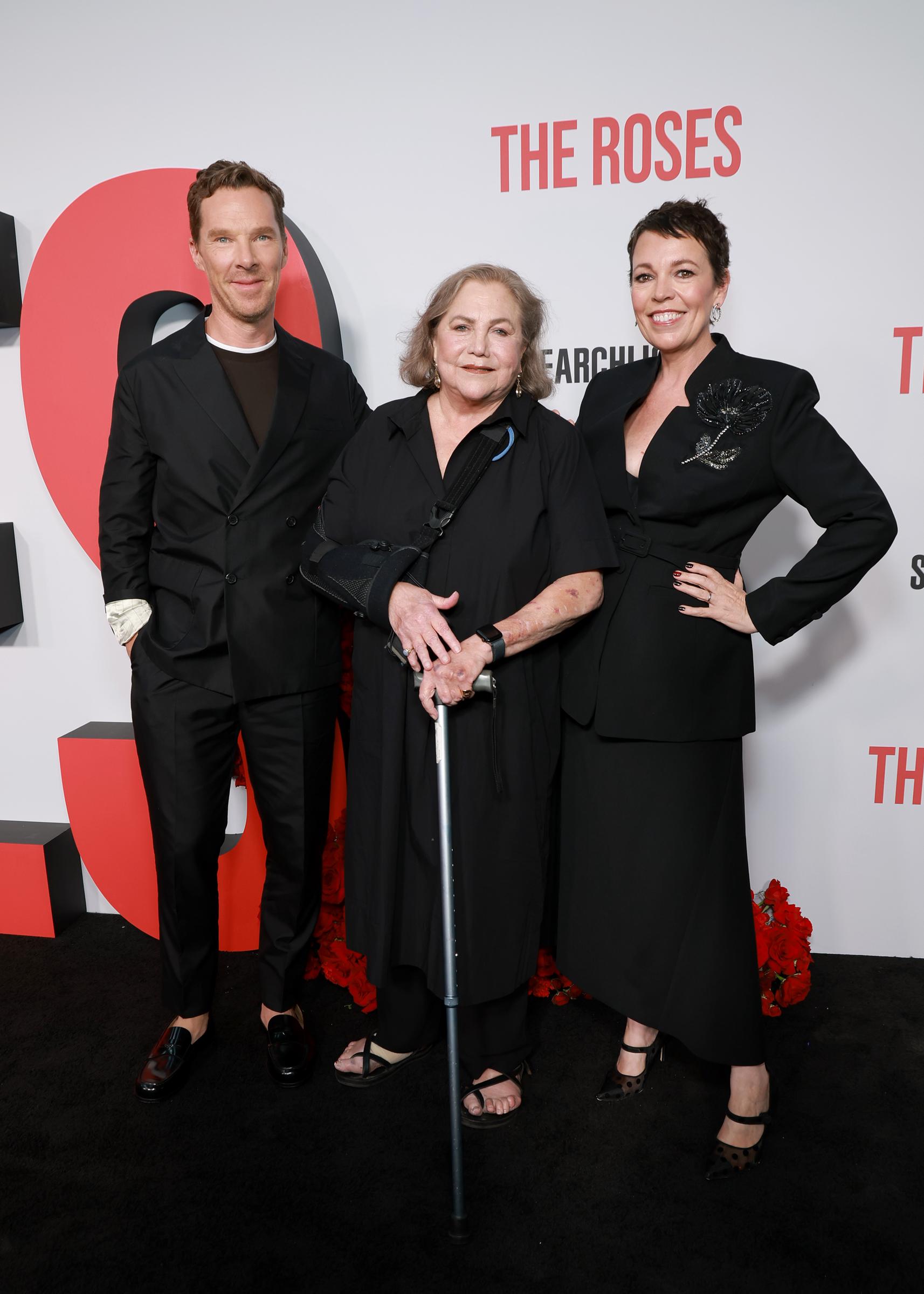 Kathleen Turner, Benedict Cumberbatch, and Olivia Colman share a warm moment on the red carpet at "The Roses" premiere at The Hudson Theater in New York City. Turner, poised with her cane, stands alongside Cumberbatch's sharp tailoring and Colman's chic floral blazer, forming a striking trio.