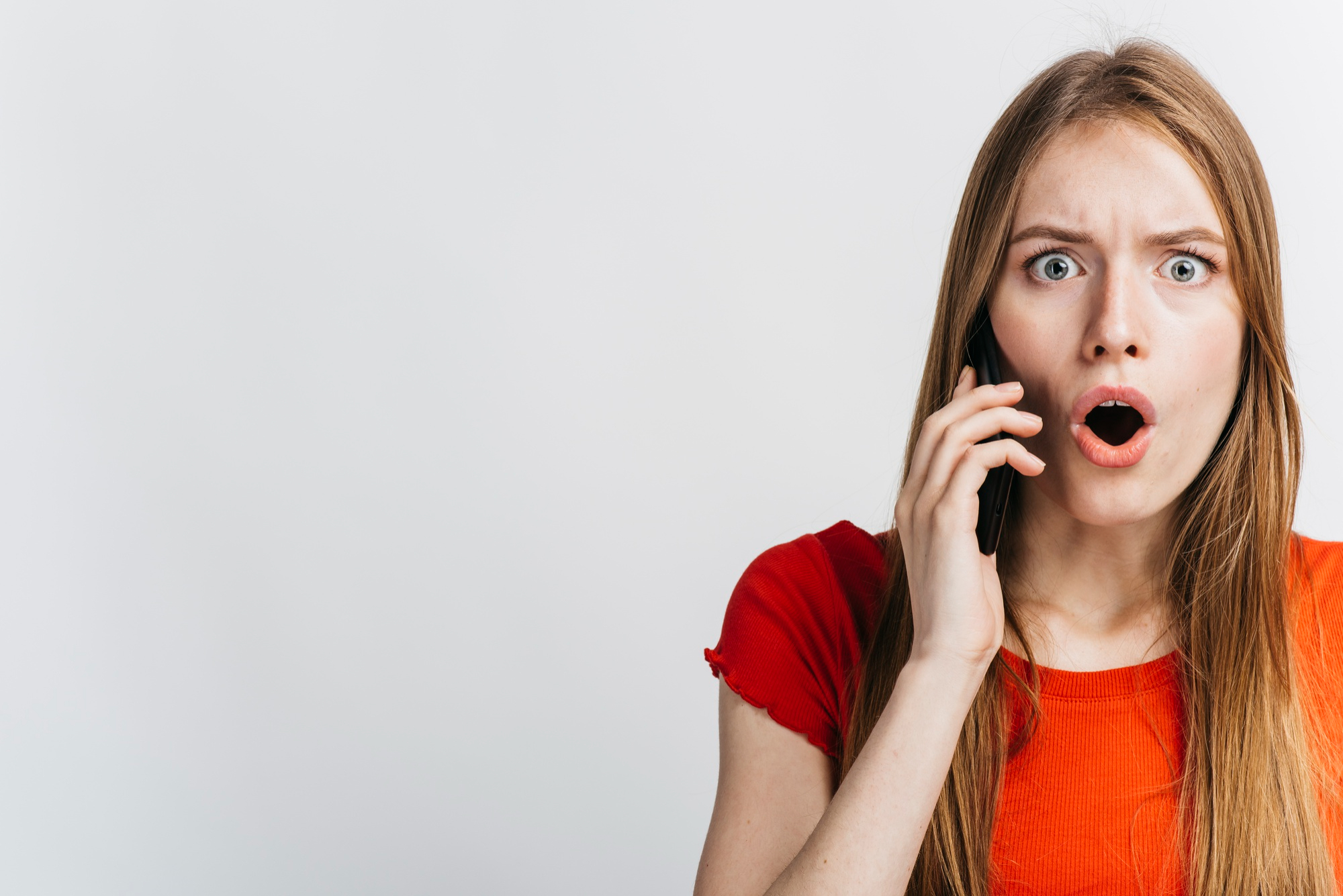 A woman reacting in shock while on a phone call | Source: Freepik