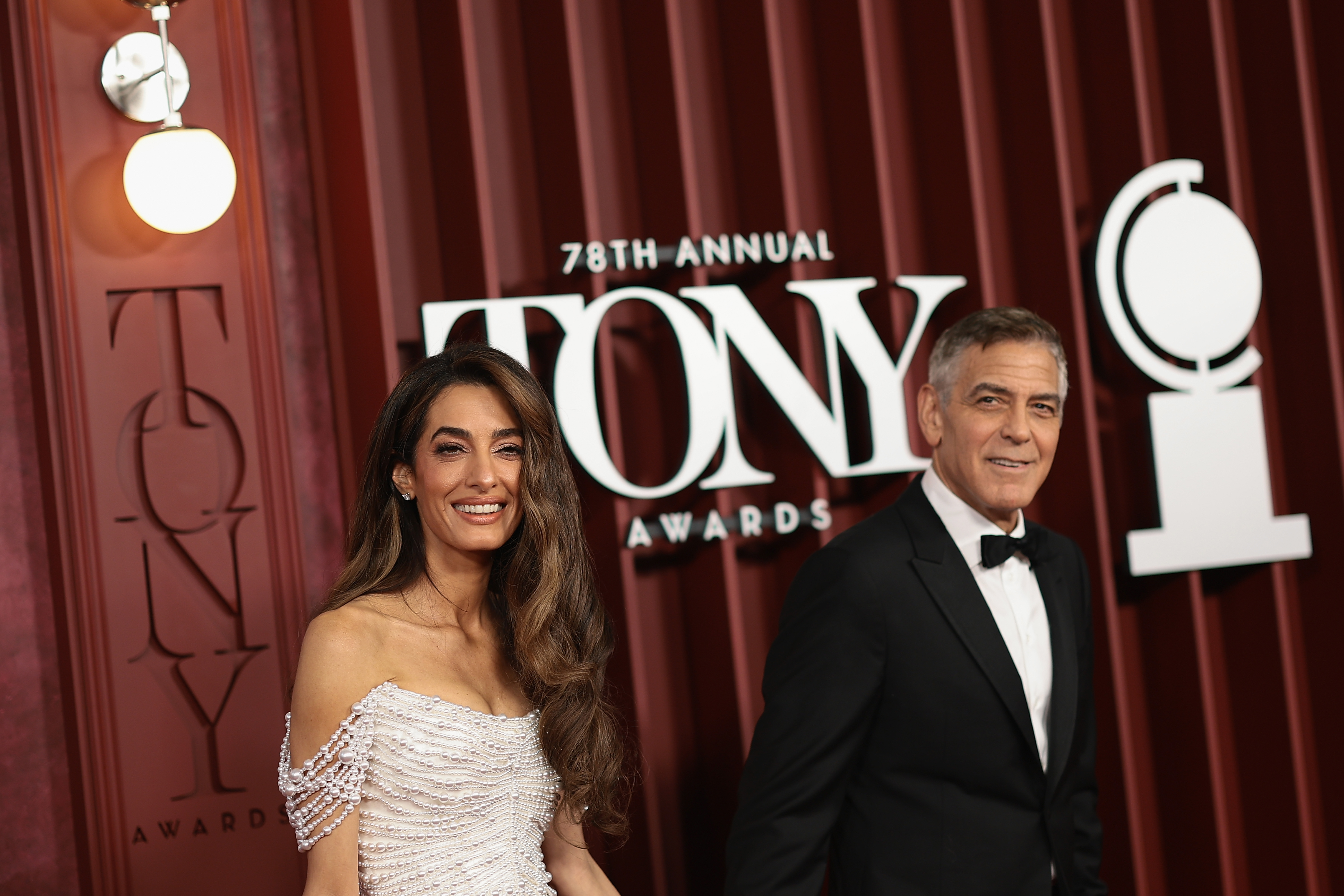 George and Amal Clooney smile side by side as they pose by the 78th Tony Awards sign. The couple's confident presence adds a touch of Hollywood charm to Broadway's big night.