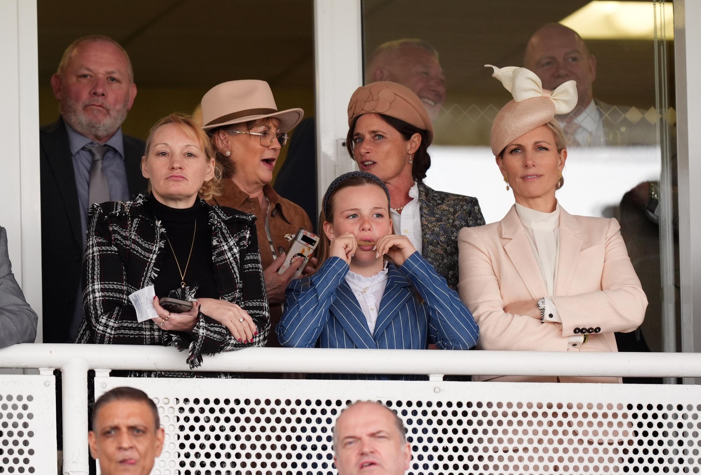 From the stands, Mia Tindall appeared fully immersed in the day's events, leaning forward with curiosity as Zara Tindall stood composed beside her, arms folded &mdash; a contrast between youthful excitement and seasoned race-day poise captured in a single frame.
