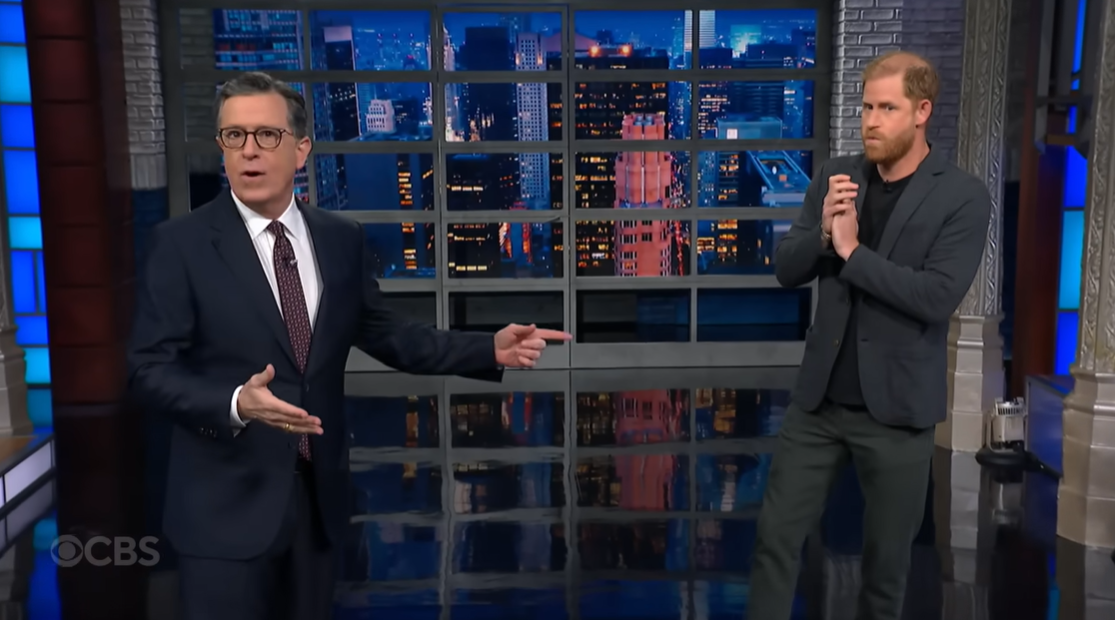 Stephen Colbert reacts with surprise as Prince Harry stands behind him, hands clasped, mid-sketch, as posted on December 4, 2025 | Source: YouTube/ColbertLateShow