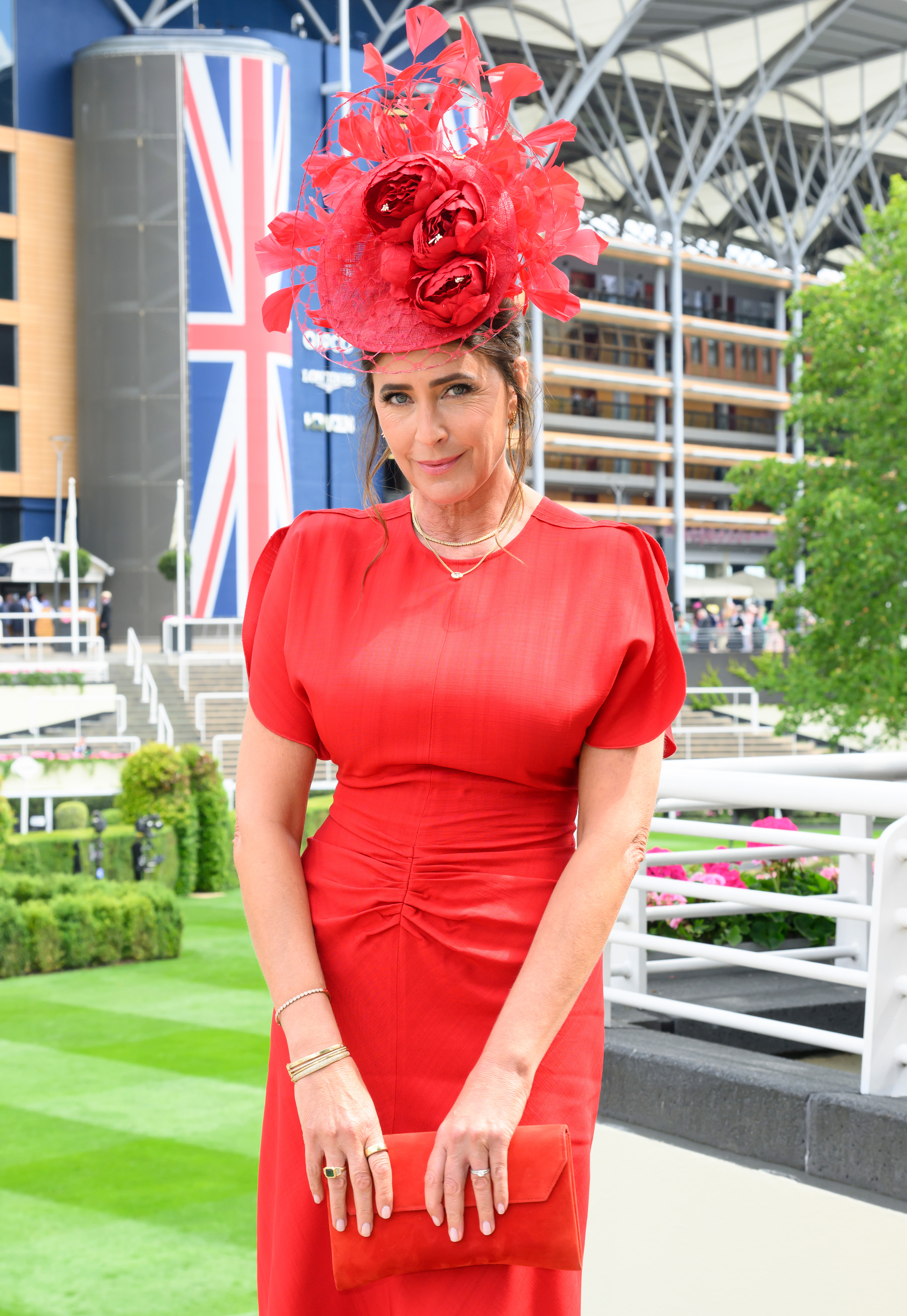 Royal Ascot, Day Two, 19 June 2024 — Dressed head-to-toe in red against the backdrop of the Ascot grandstand and a Union Jack flag, Snowdon wears a structured puff-sleeved midi dress and carries a matching red clutch, topped with an extravagant red floral and feather fascinator.