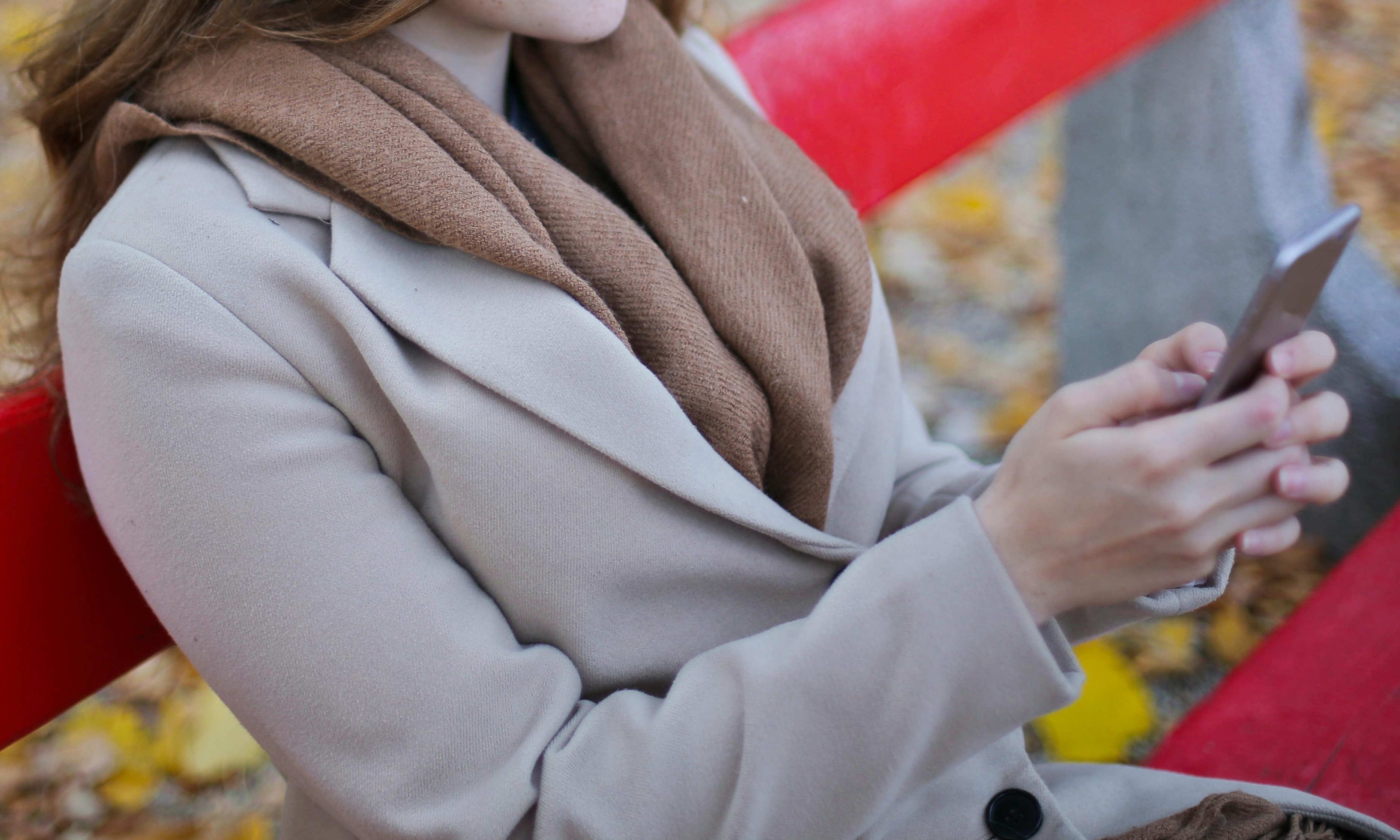 An woman sitting on a park bench with a cell phone in her hands | Source: Pexels