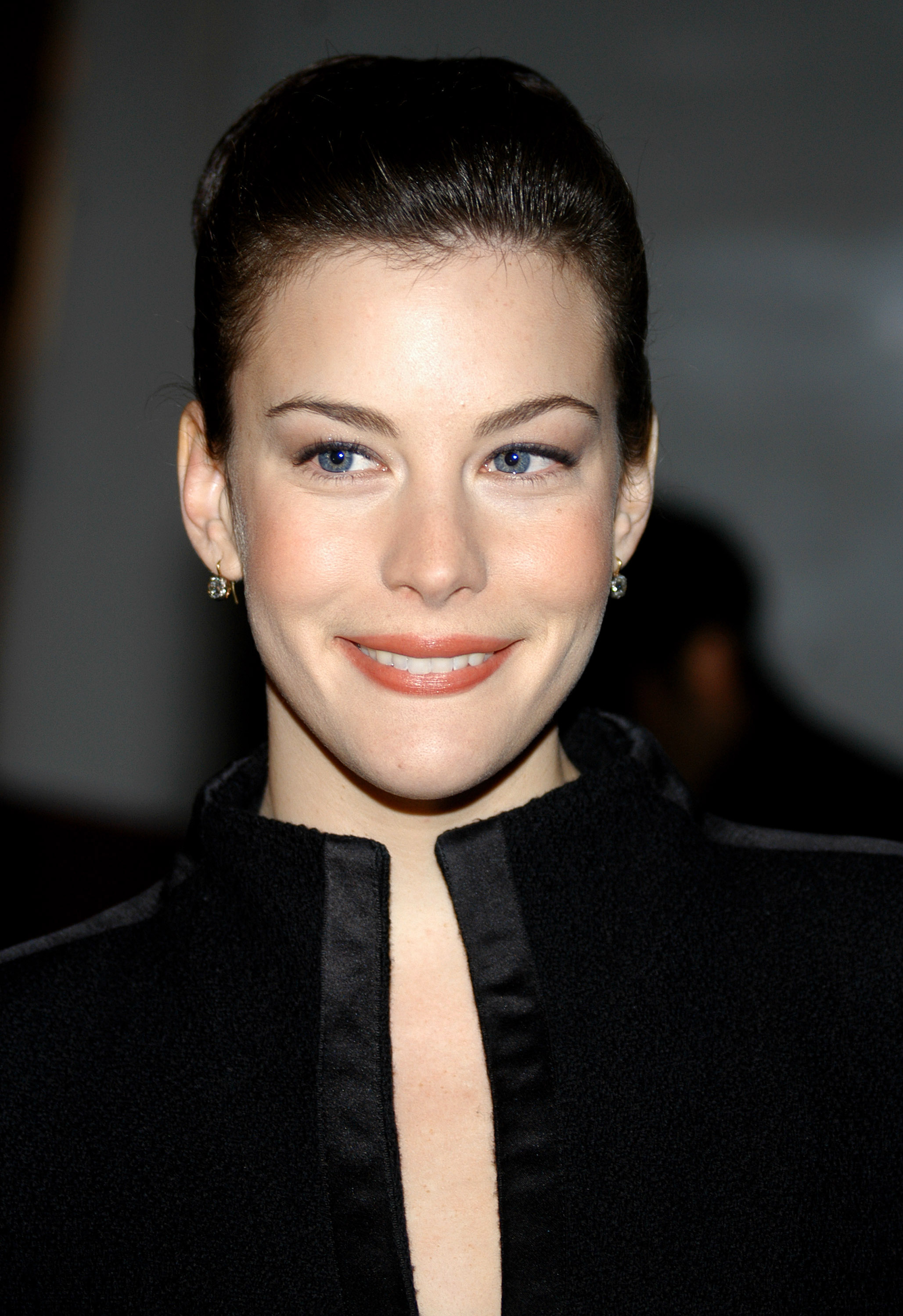 Liv Tyler attends the first annual UNICEF Snowflake Lighting Ceremony in 2003 in front of the Plaza Hotel in New York City, wearing a sleek black outfit with her hair pulled back, her soft smile and bright eyes giving her a polished, elegant look.