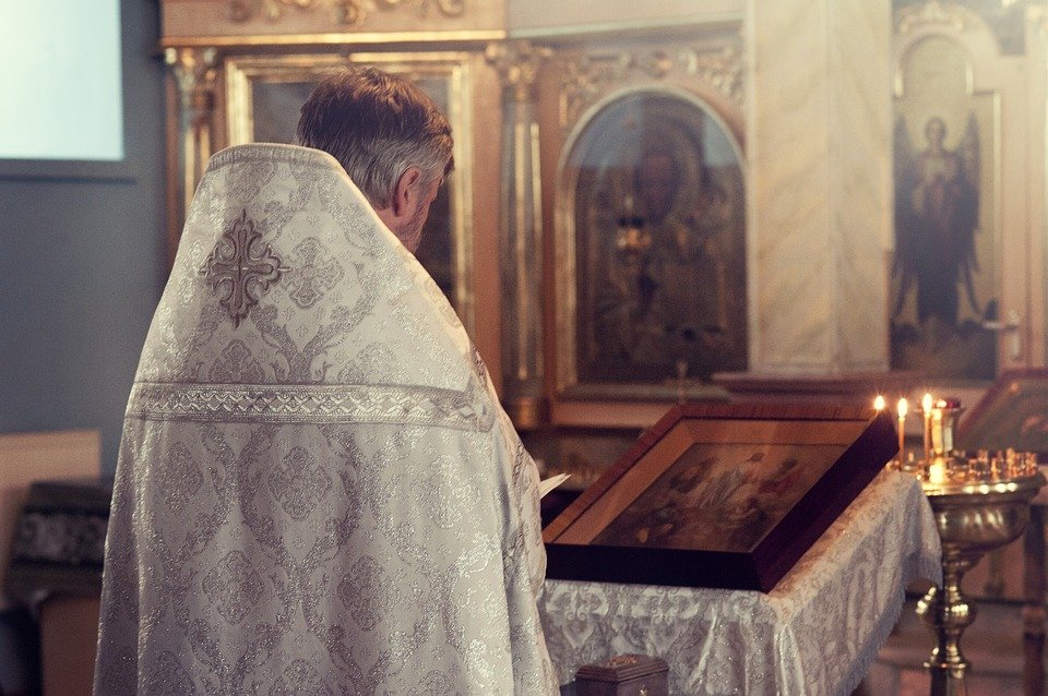 A Priest faces the altar while reading from a book in a Church | Photo: Pixabay