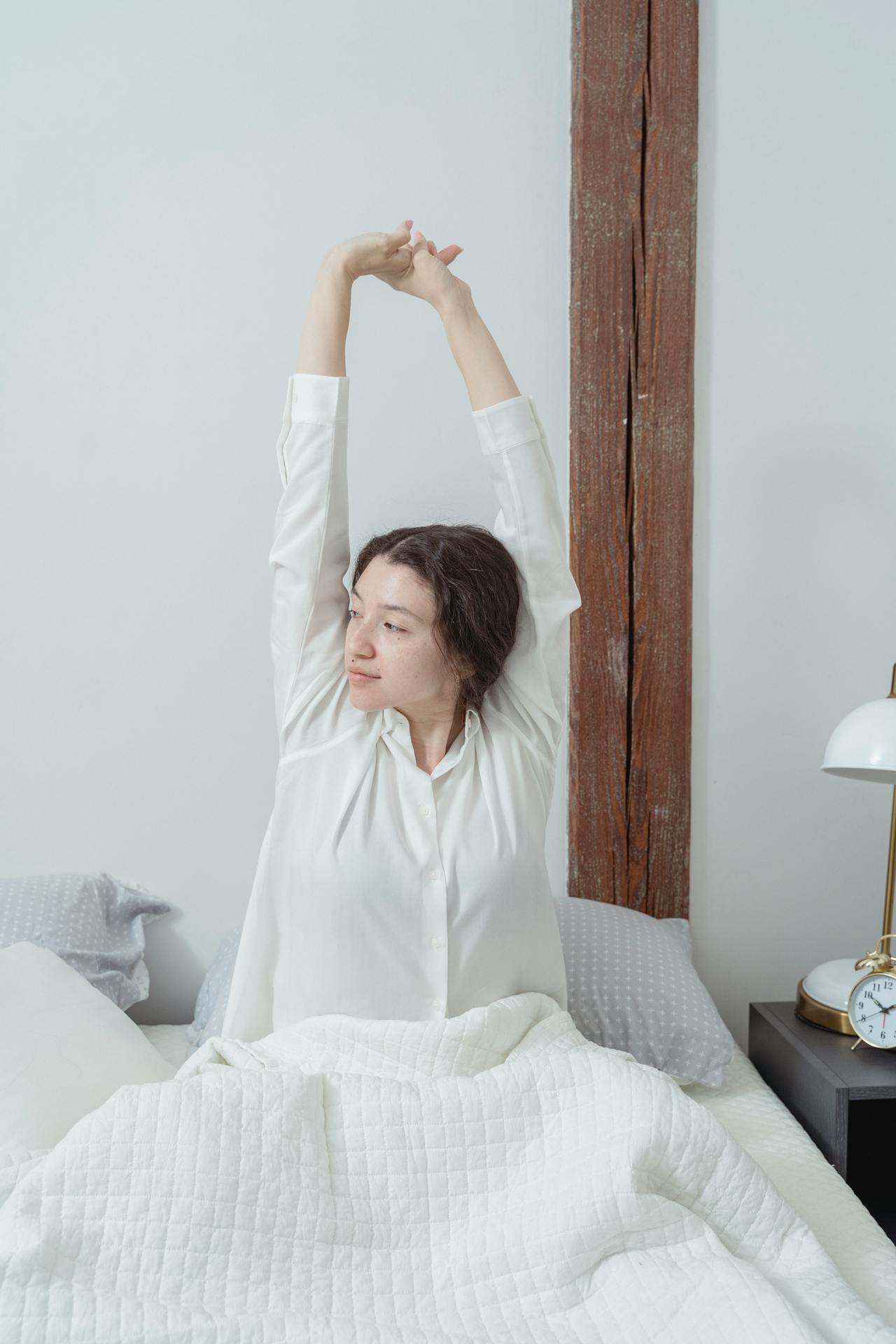 A woman stretching her arms while sitting on the bed | Source: Pexels