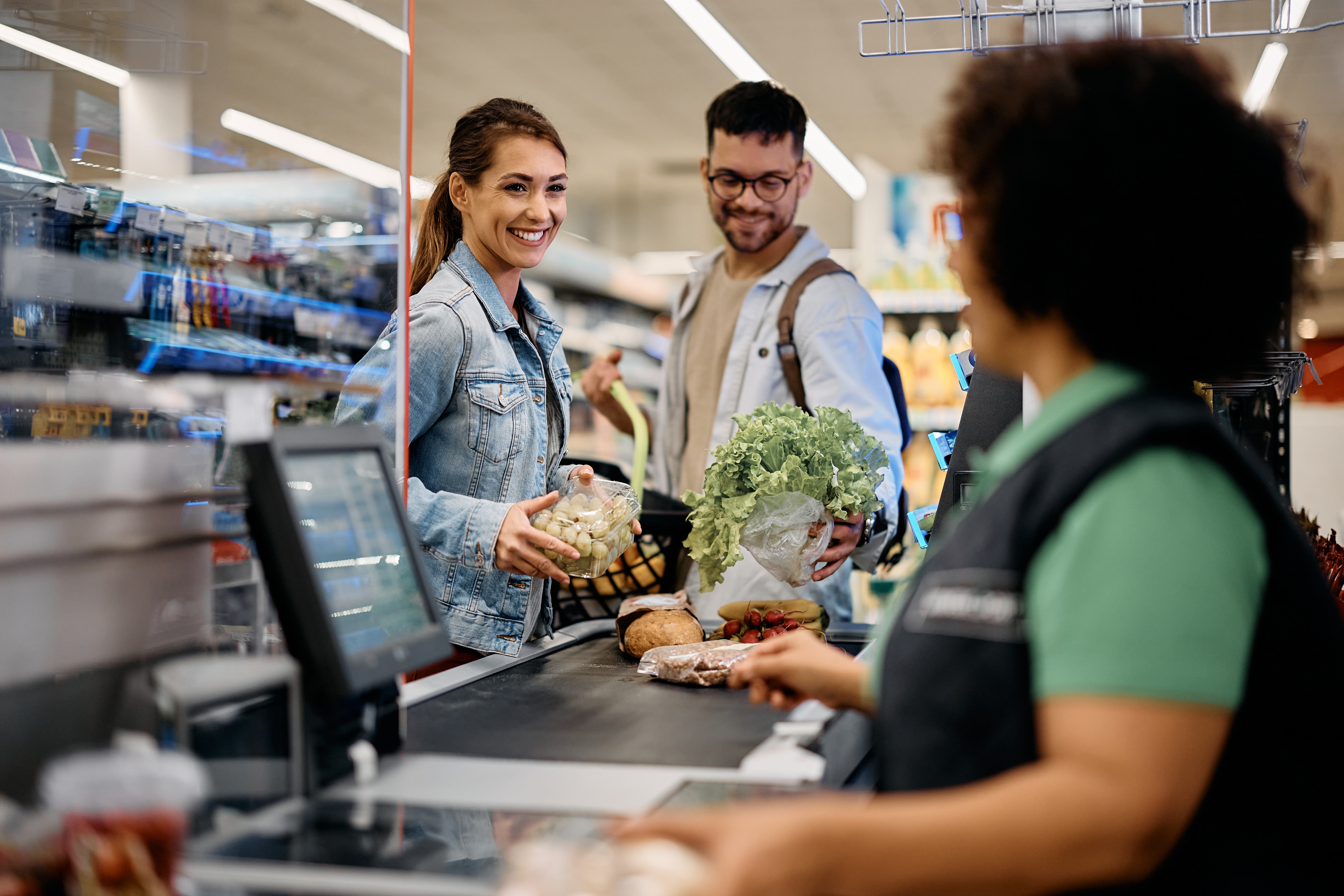 Happy couple talking to cahier while putting groceries on checkout counter in the supermarket | Source: Shutterstock