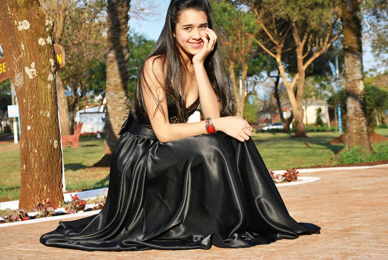 Mujer de cuclillas usando un vestido largo negro mientras posa en un parque. | Foto: Needpix.com