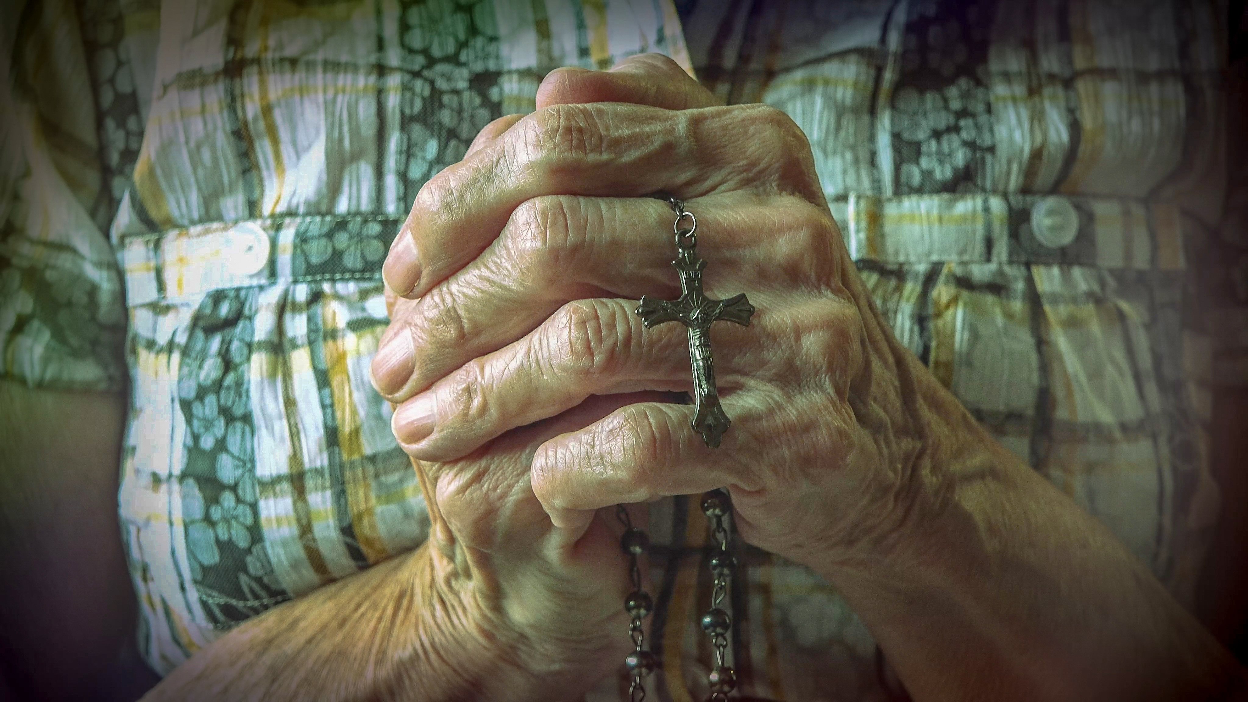 Elderly woman's hands holding a necklace with a cross | Photo: Shutterstock