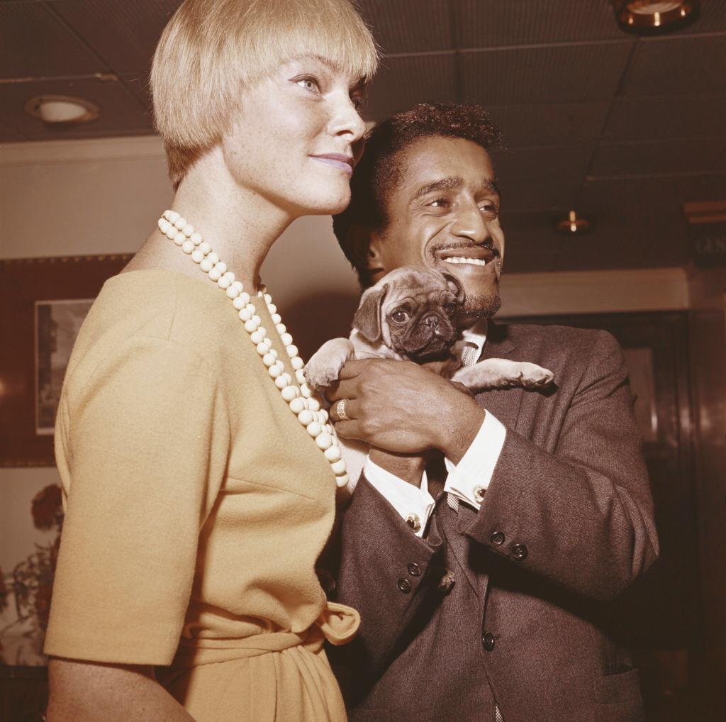 American singer, actor and comedian Sammy Davis Jr (1925-1990) pictured holding a Pug dog with his wife, Swedish actress May Britt in England in 1961 | Photo: Getty Images