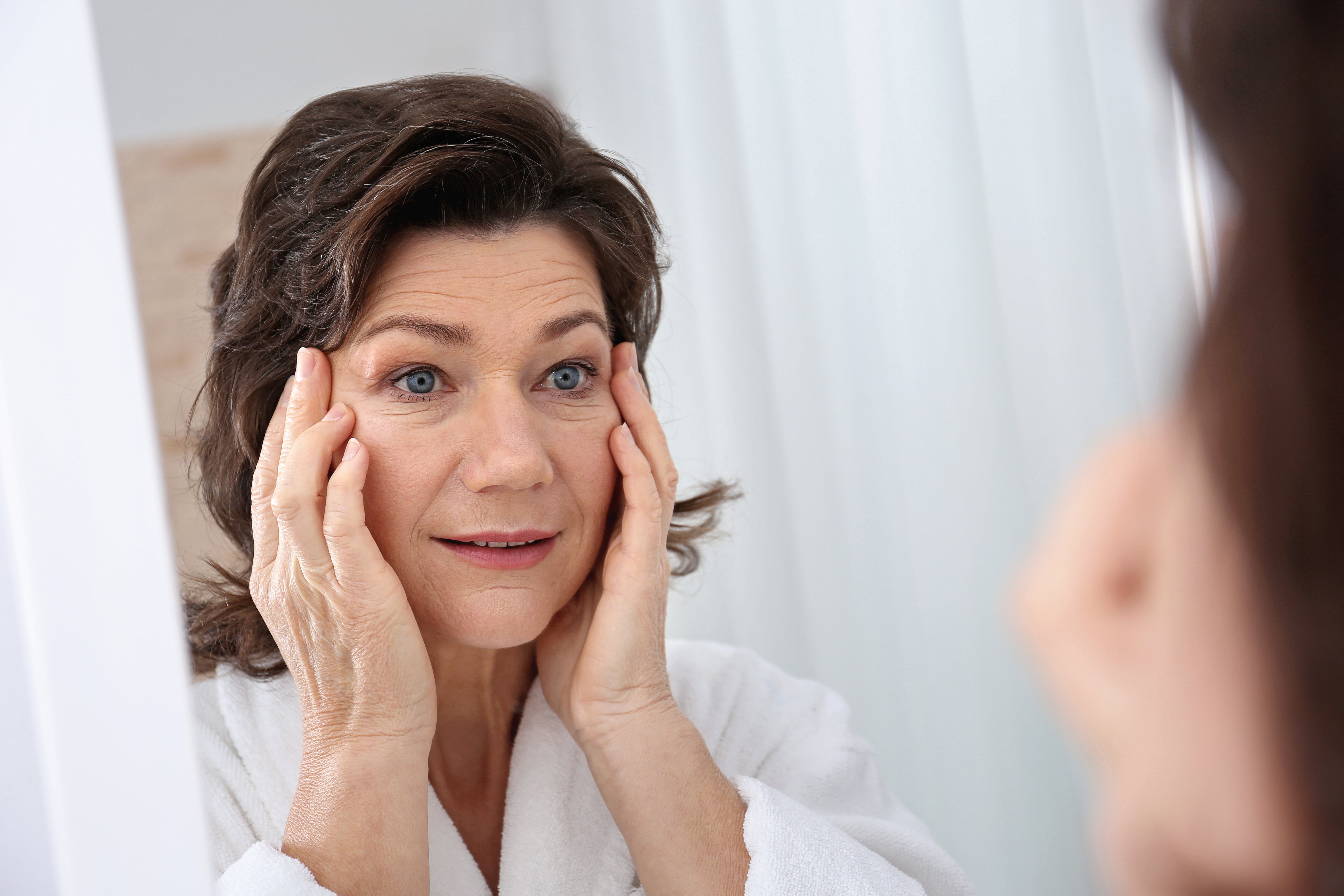 A closeup photo of a woman touching her face in front of mirror. | Photo: Shutterstock