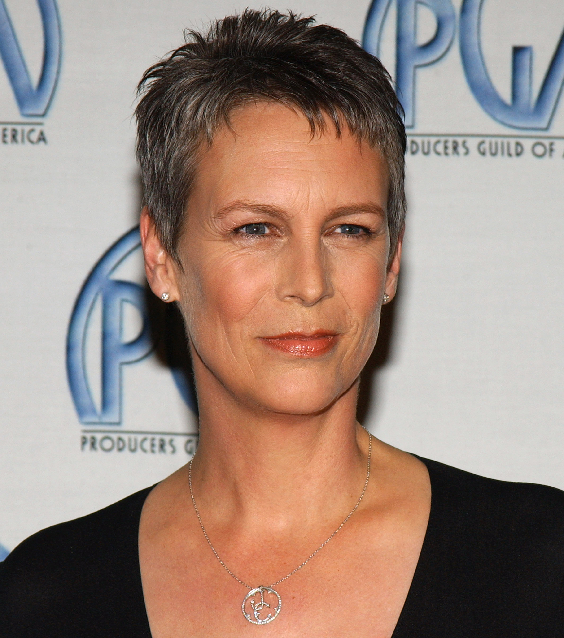 Jamie Lee Curtis arrives at the 15th Annual Producers Guild Awards in Century City with confident elegance, wearing a sleek black top, peace-symbol pendant necklace, and her signature salt-and-pepper pixie cut styled to perfection.